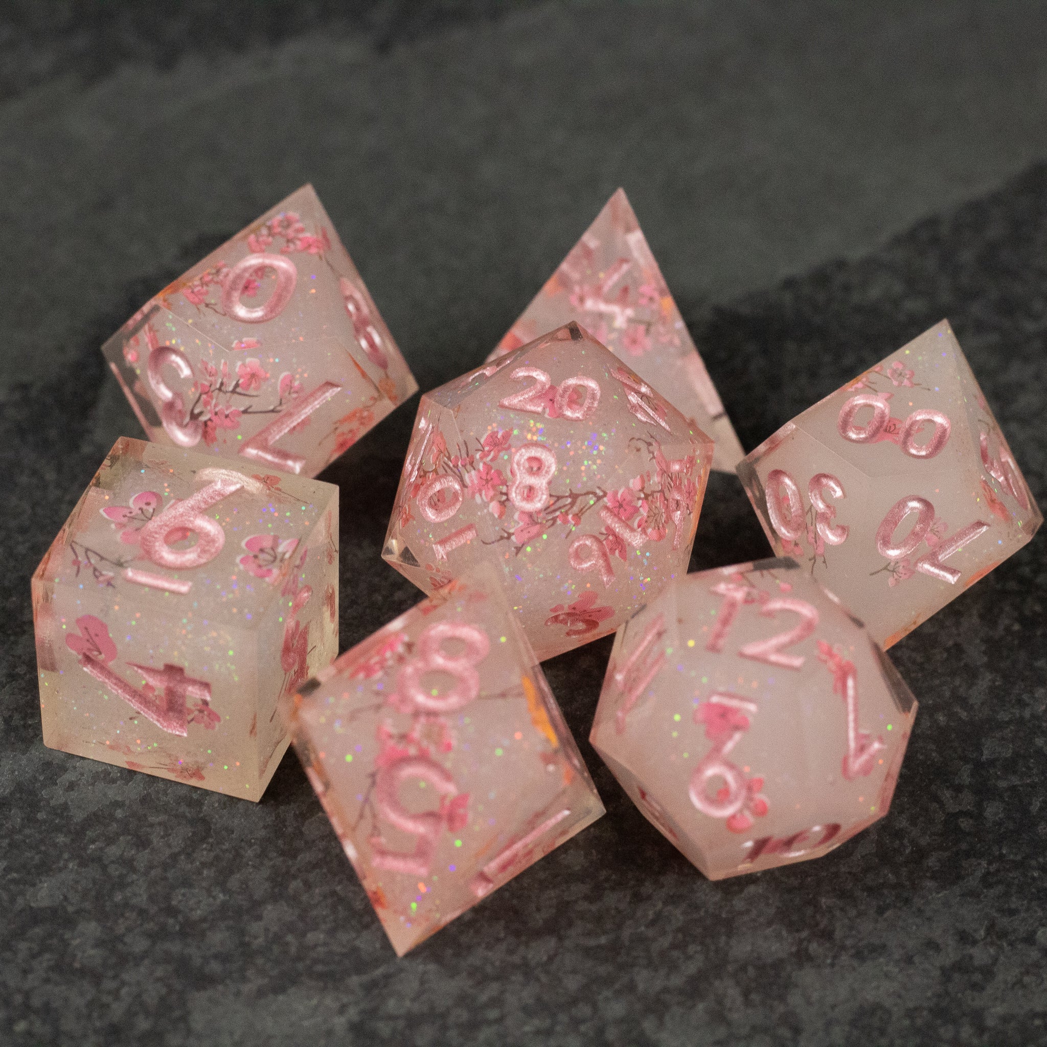 Pink Cherry Blossom Dice Set - Translucent pink seven-piece sharp-edged dice set with cherry blossom inclusions and pink numbering.