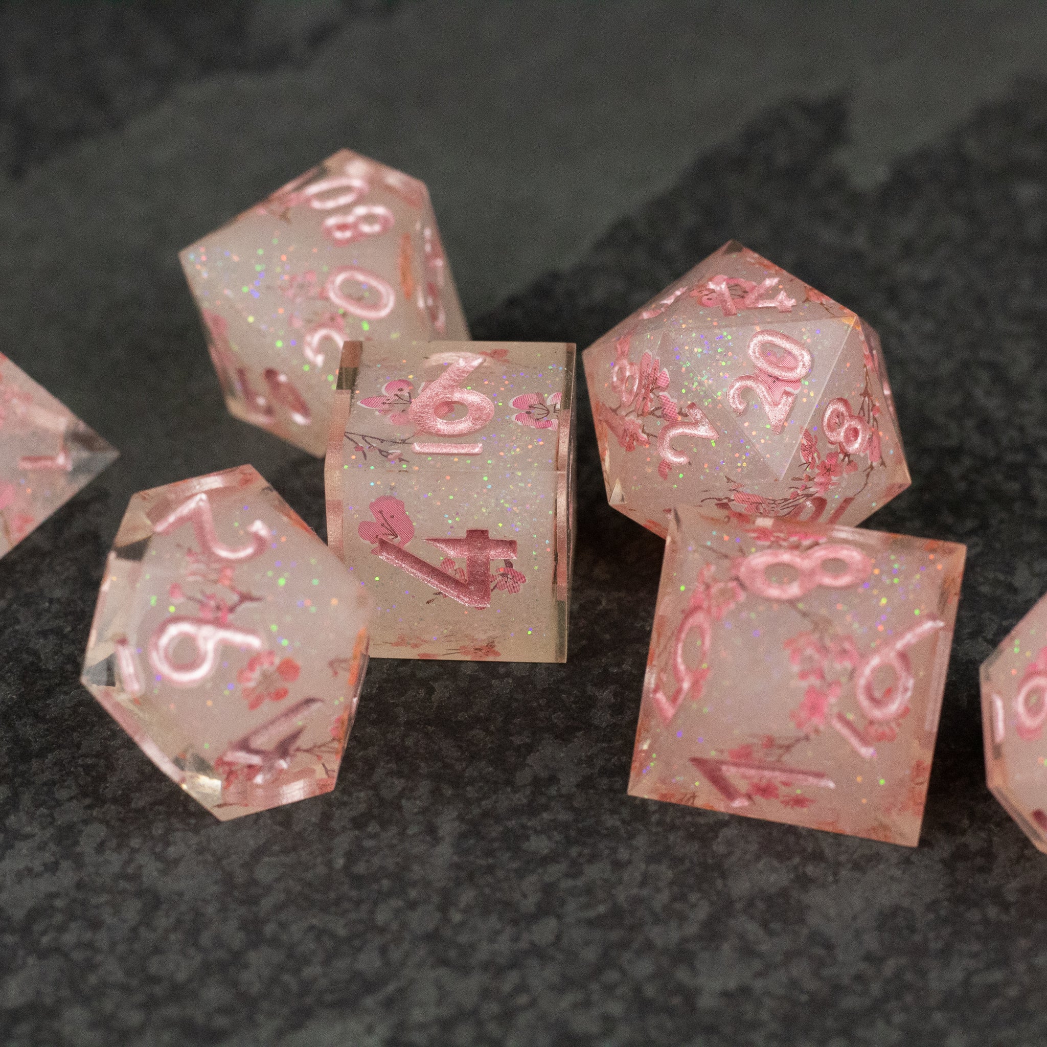 Pink Cherry Blossom Dice Set - Translucent pink seven-piece dice set with sharp edges, featuring embedded cherry blossom petals and white numbering.