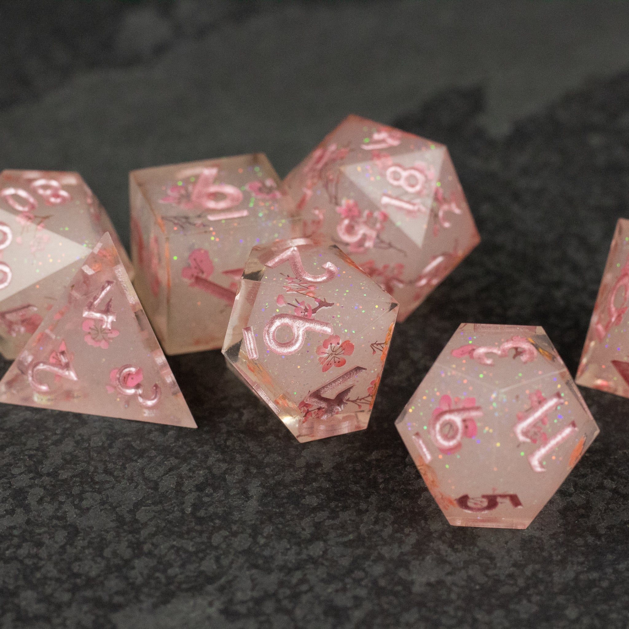 Pink Cherry Blossom Dice Set - Translucent pink 7-piece sharp-edged dice set with embedded cherry blossom flakes and white numbers.