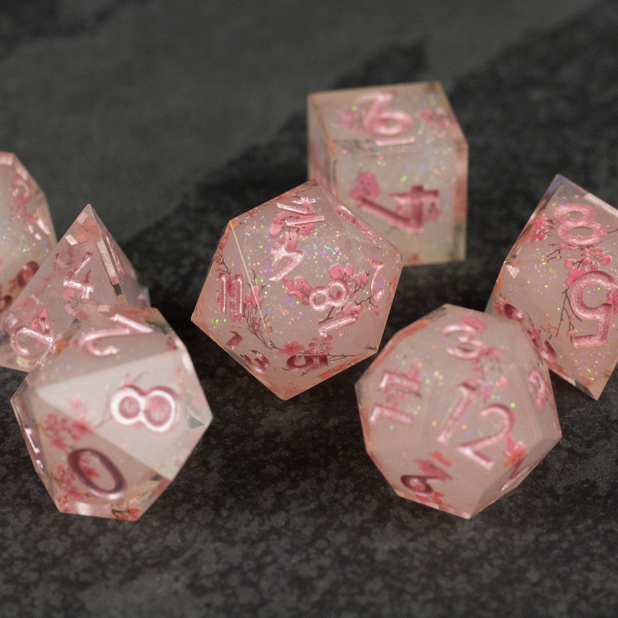 Pink Cherry Blossom Dice Set - Translucent pink sharp-edged polyhedral dice with pink cherry blossom petals and white numbering.