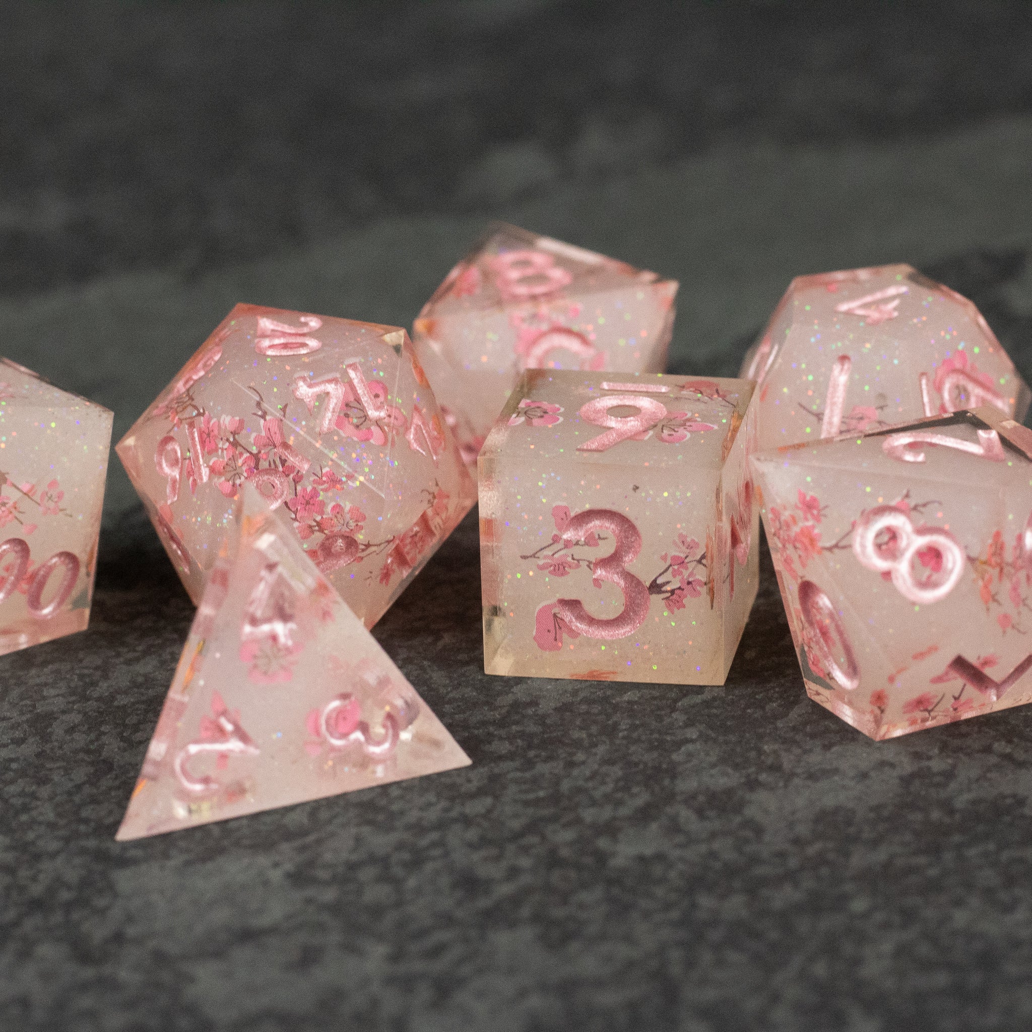 Pink Cherry Blossom Dice Set - Translucent pink sharp-edged dice set with embedded cherry blossom petals, various polyhedral shapes.