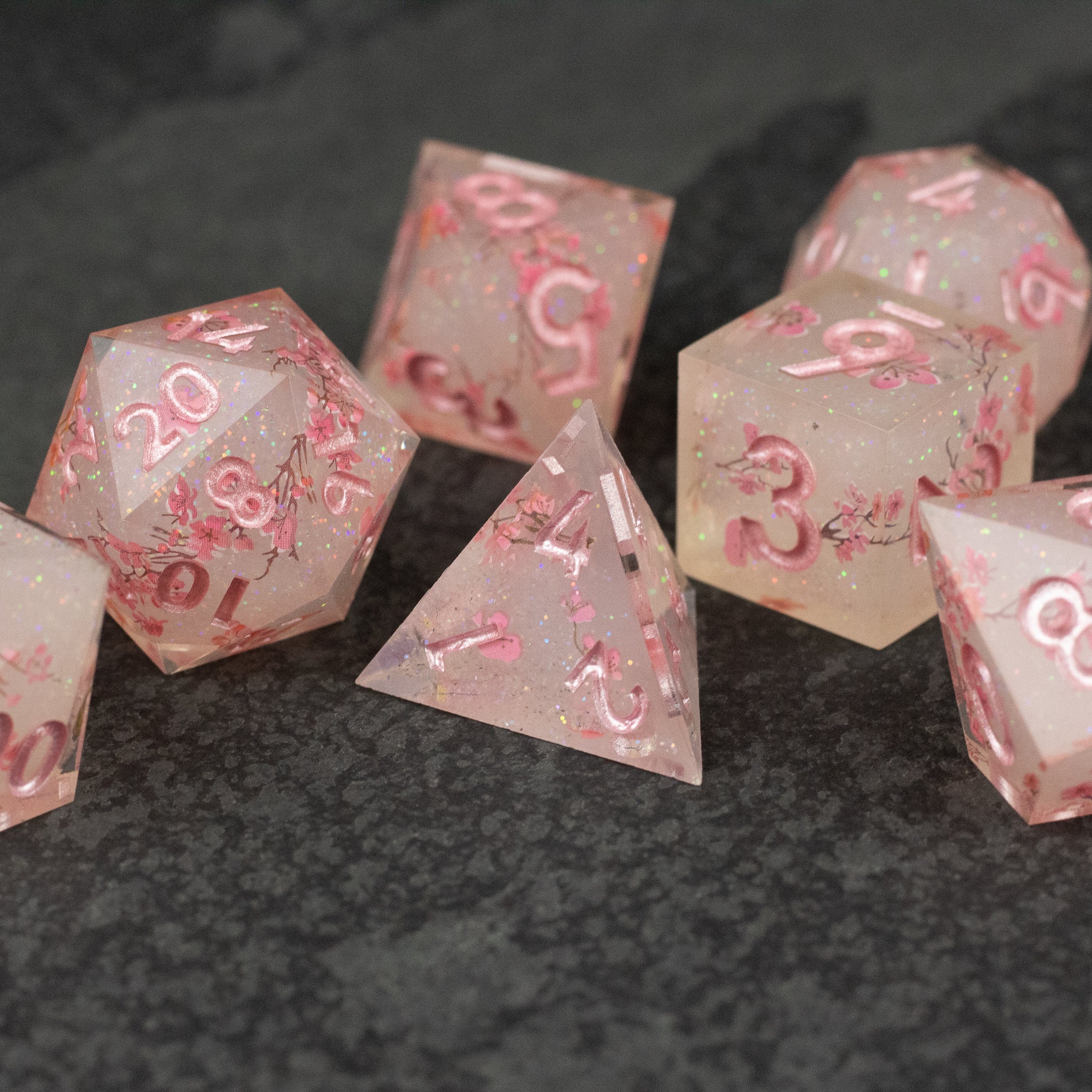 Pink Cherry Blossom Dice Set - Translucent pink sharp-edged polyhedral dice set with cherry blossom inclusions and pink numbering.