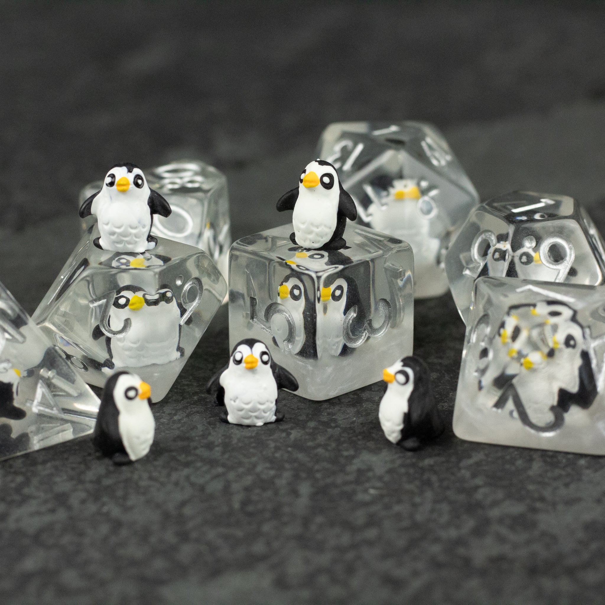 Penguin Dice Set - Clear polyhedral dice with small, detailed penguin figures inside each die on dark textured surface.