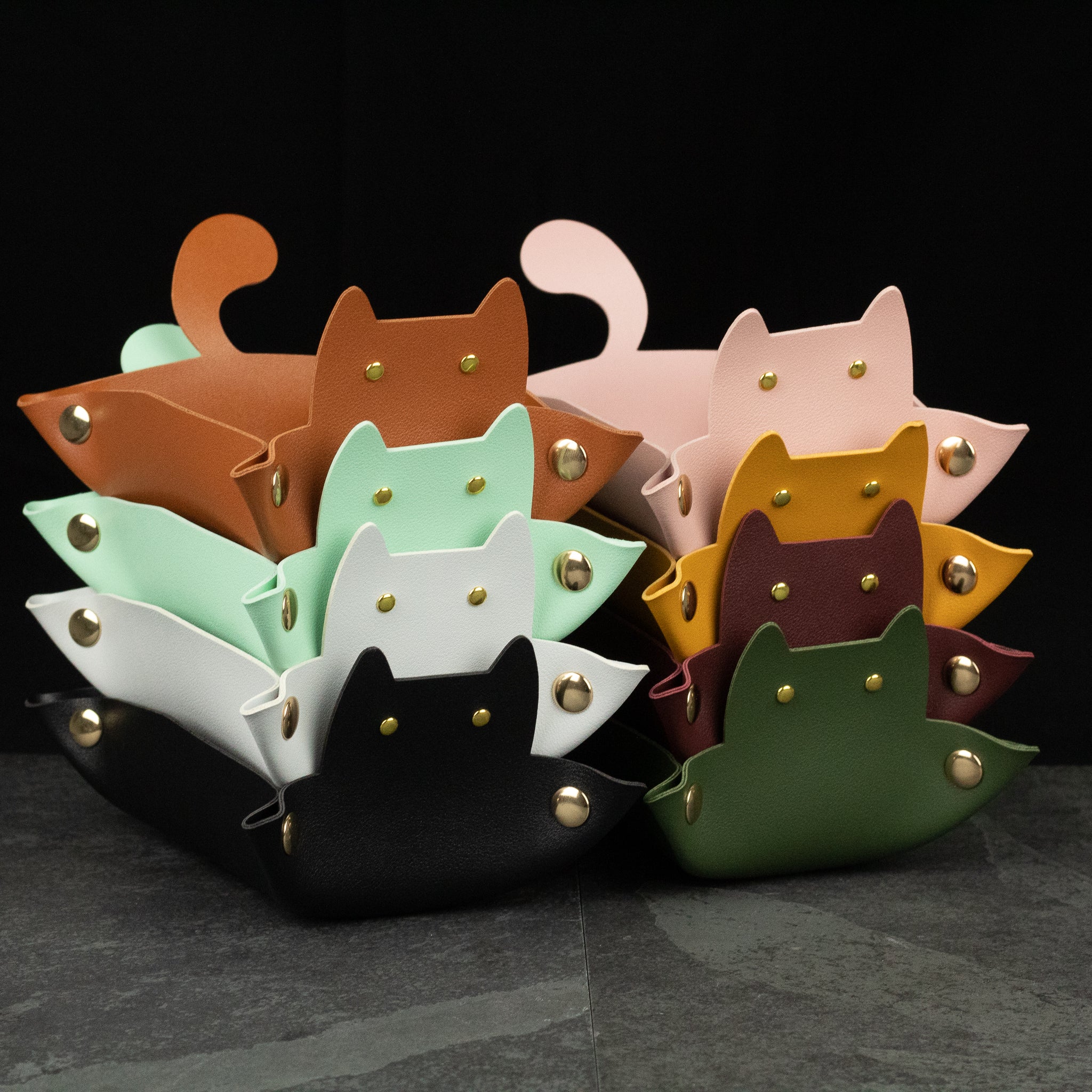 Cat Shaped Dice Tray - Stack of leather cat-shaped dice trays in various colors including mint, pink, tan, mustard, burgundy, black, and green with .