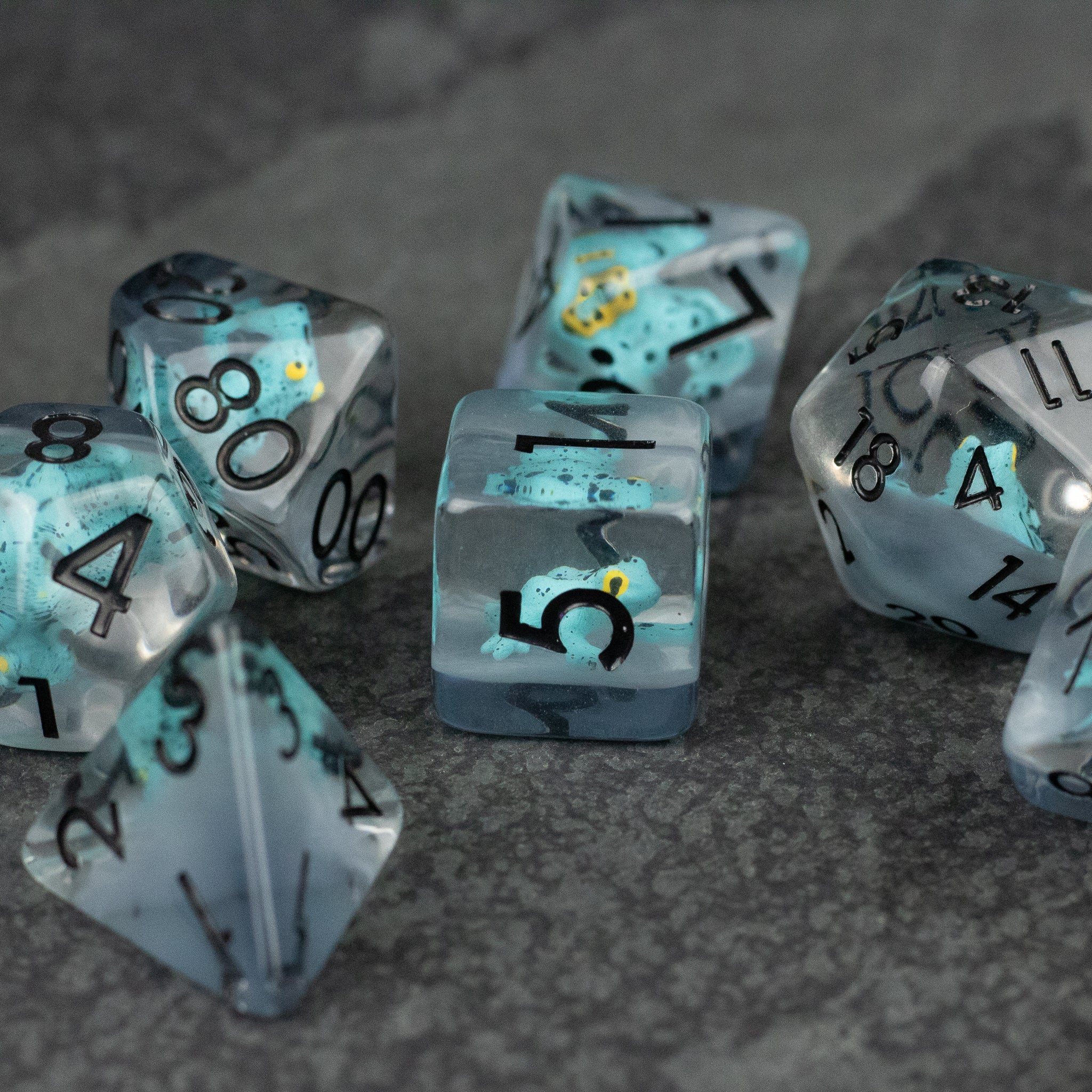 Blue Frog Dice Set - Translucent blue polyhedral dice set with black numbers and yellow frog inclusions on gray surface.