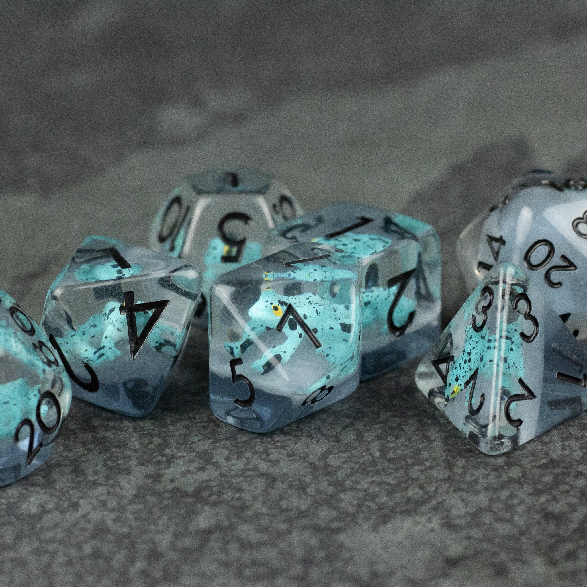 Blue Frog Dice Set - Translucent blue polyhedral dice set with black numbers and embedded frog silhouettes on a gray surface.