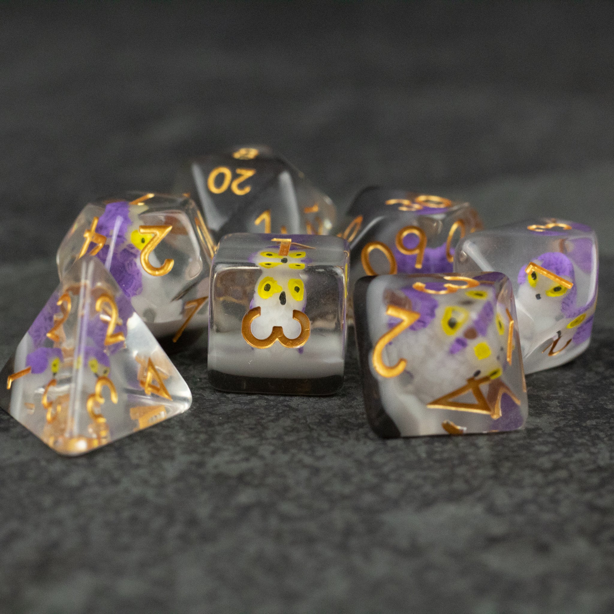 Purple Owl Dice Set - Seven translucent purple and gray polyhedral dice with gold numbers and an owl face on the d20 die.