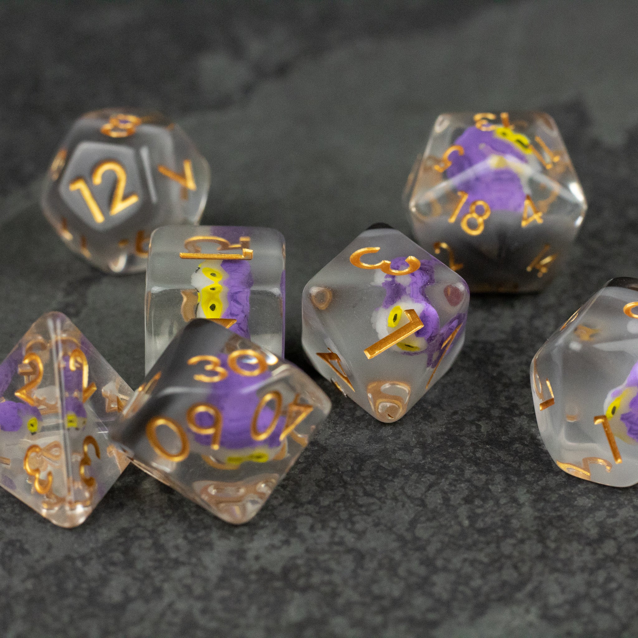 Purple Owl Dice Set - Set of translucent polyhedral dice with purple and gold swirls and gold numbering on dark background.