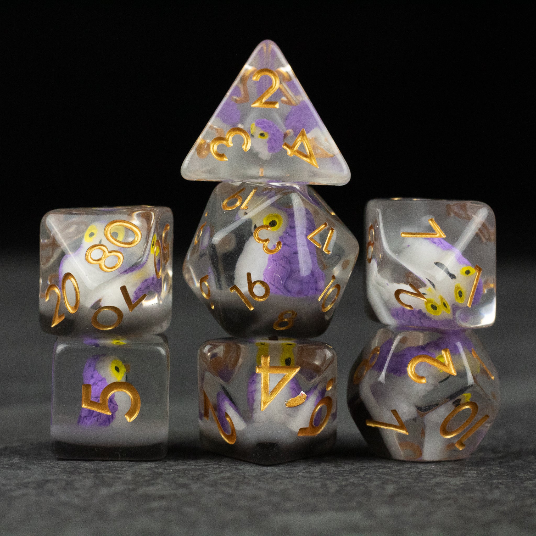 Purple Owl Dice Set - Set of seven translucent dice with purple and white swirls, gold numbering, shaped for various tabletop games.
