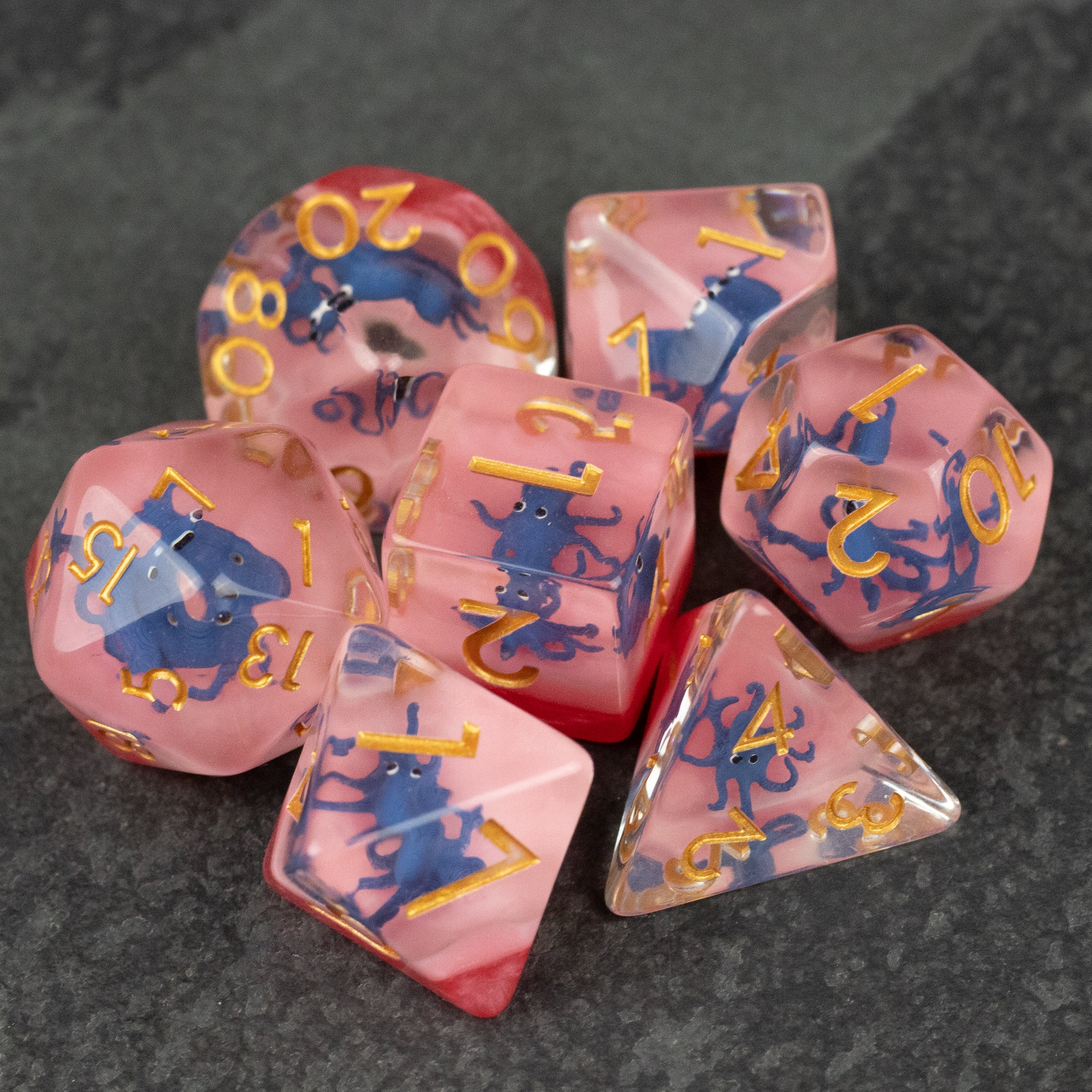 Dark Blue Octopus Dice Set - Seven pink translucent polyhedral dice with gold numbers and dark blue octopus-themed designs inside.