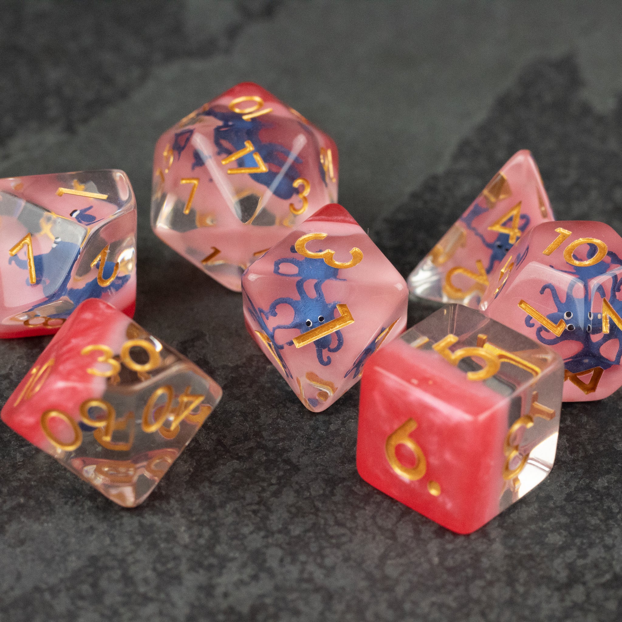 Dark Blue Octopus Dice Set - Set of transparent pink polyhedral dice with golden numbers and blue octopus illustrations inside.