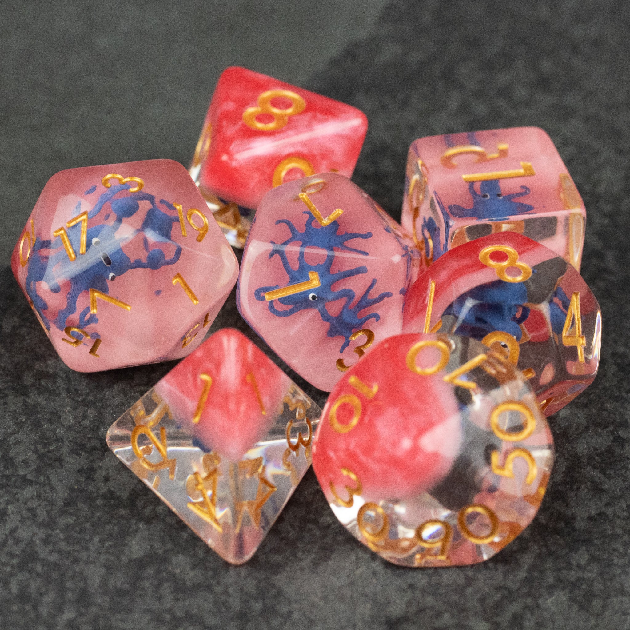 Dark Blue Octopus Dice Set - Translucent pink and red polyhedral dice set with dark blue octopus designs and gold numbers on a dark textured surface.