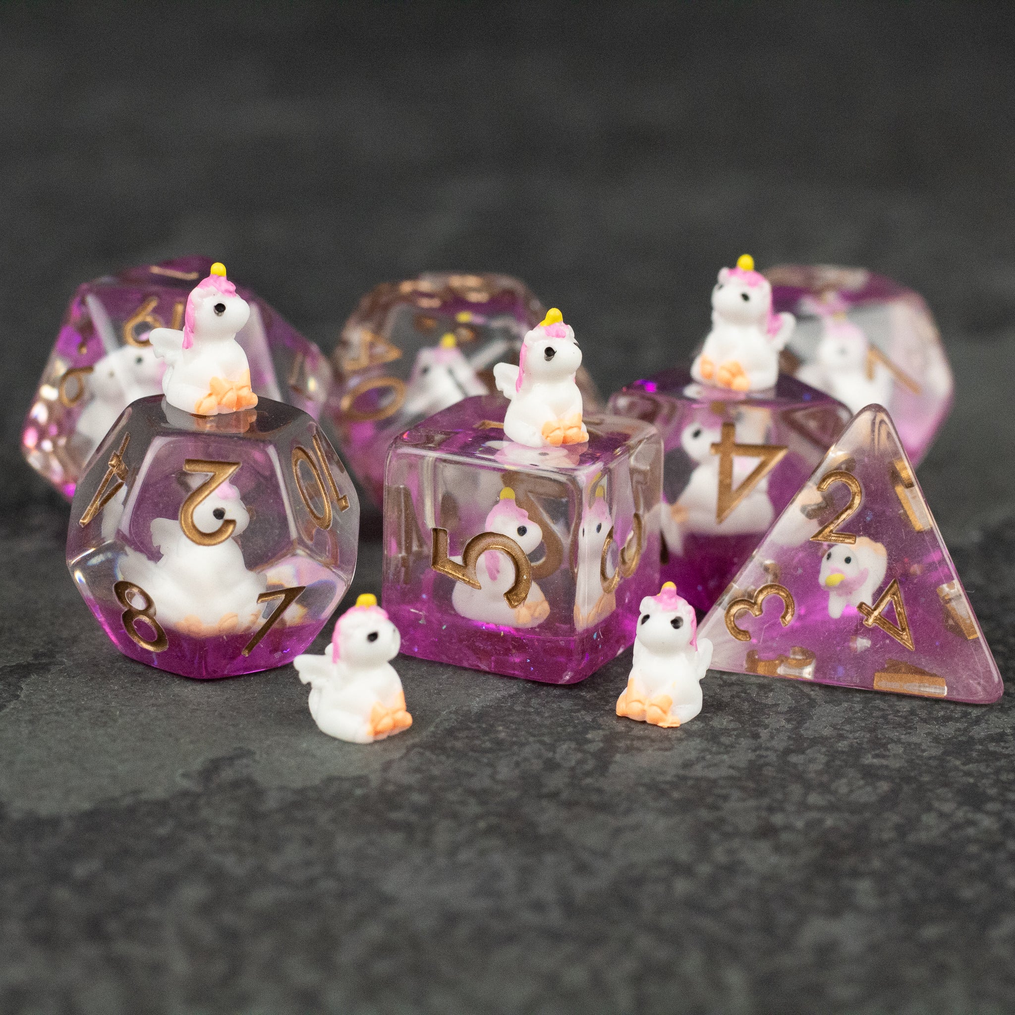 Pink Unicorn Dice Set - Transparent pink polyhedral dice set with gold numbers and small white unicorn figurines inside.
