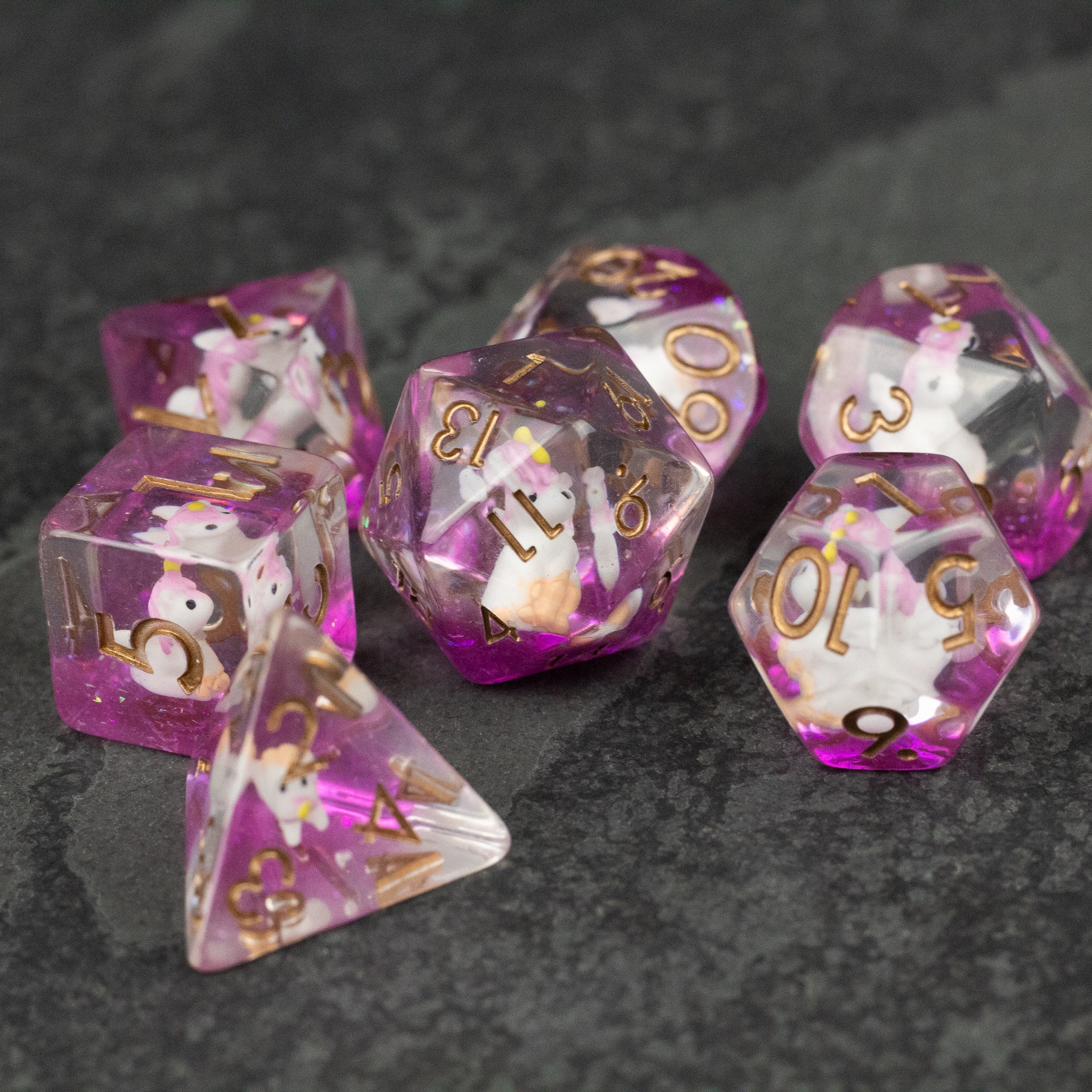 Pink Unicorn Dice Set - Purple translucent polyhedral dice set with gold numbers, each containing a small white unicorn figure inside.