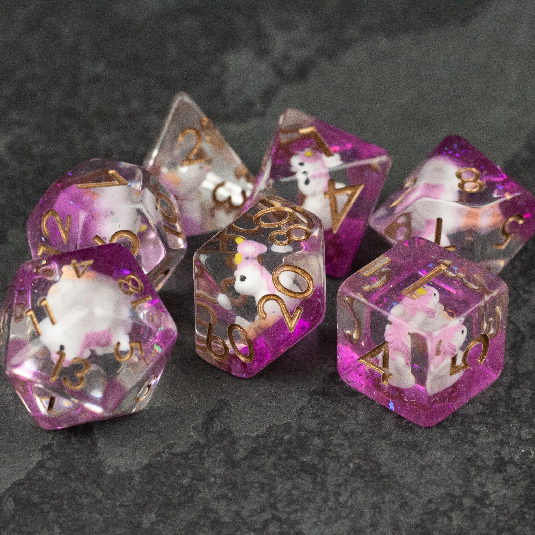 Pink Unicorn Dice Set - Translucent pink and clear polyhedral dice set with gold numbers and white unicorn illustrations.