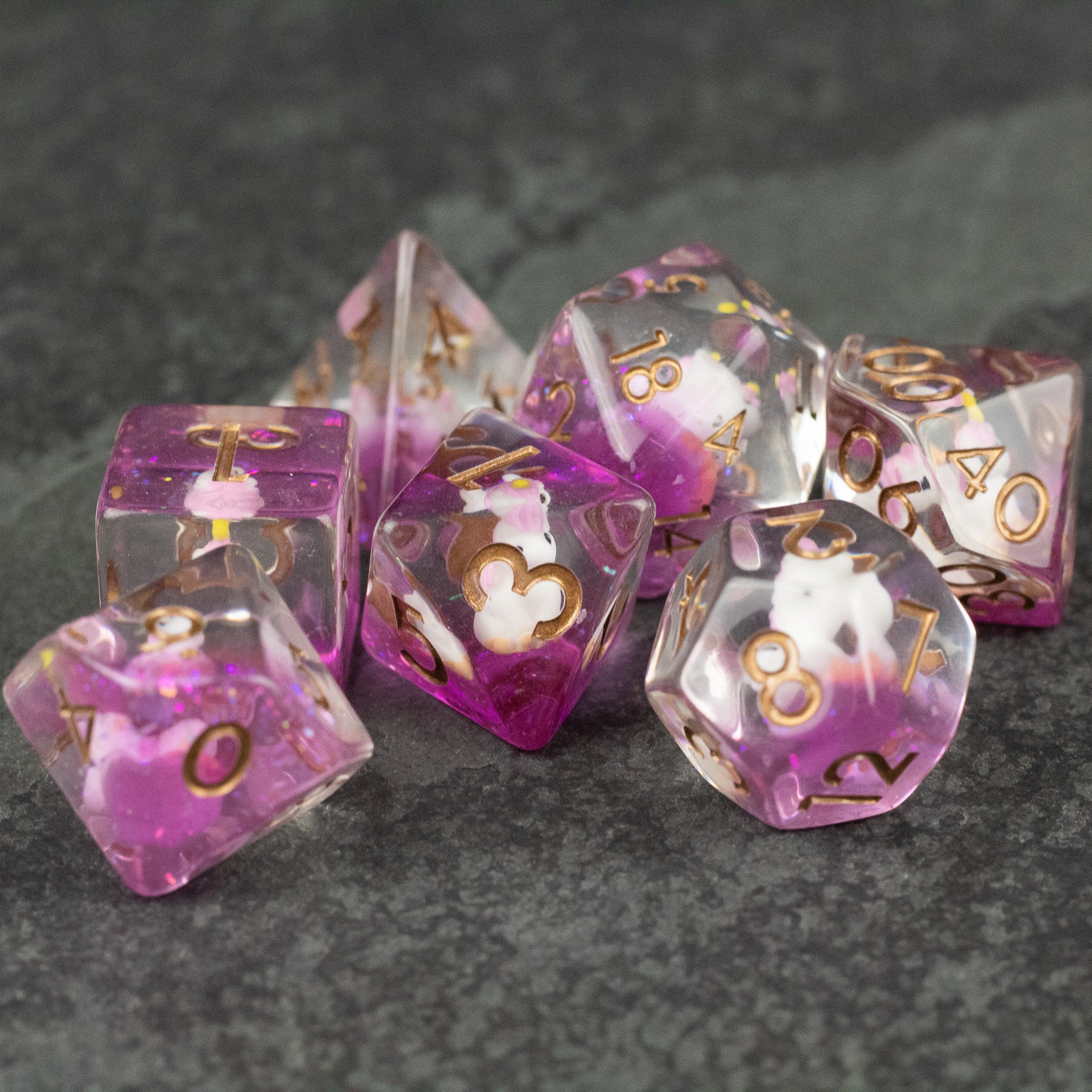 Pink Unicorn Dice Set - Set of translucent pink and clear polyhedral dice with gold numbers and white unicorn designs inside each die.