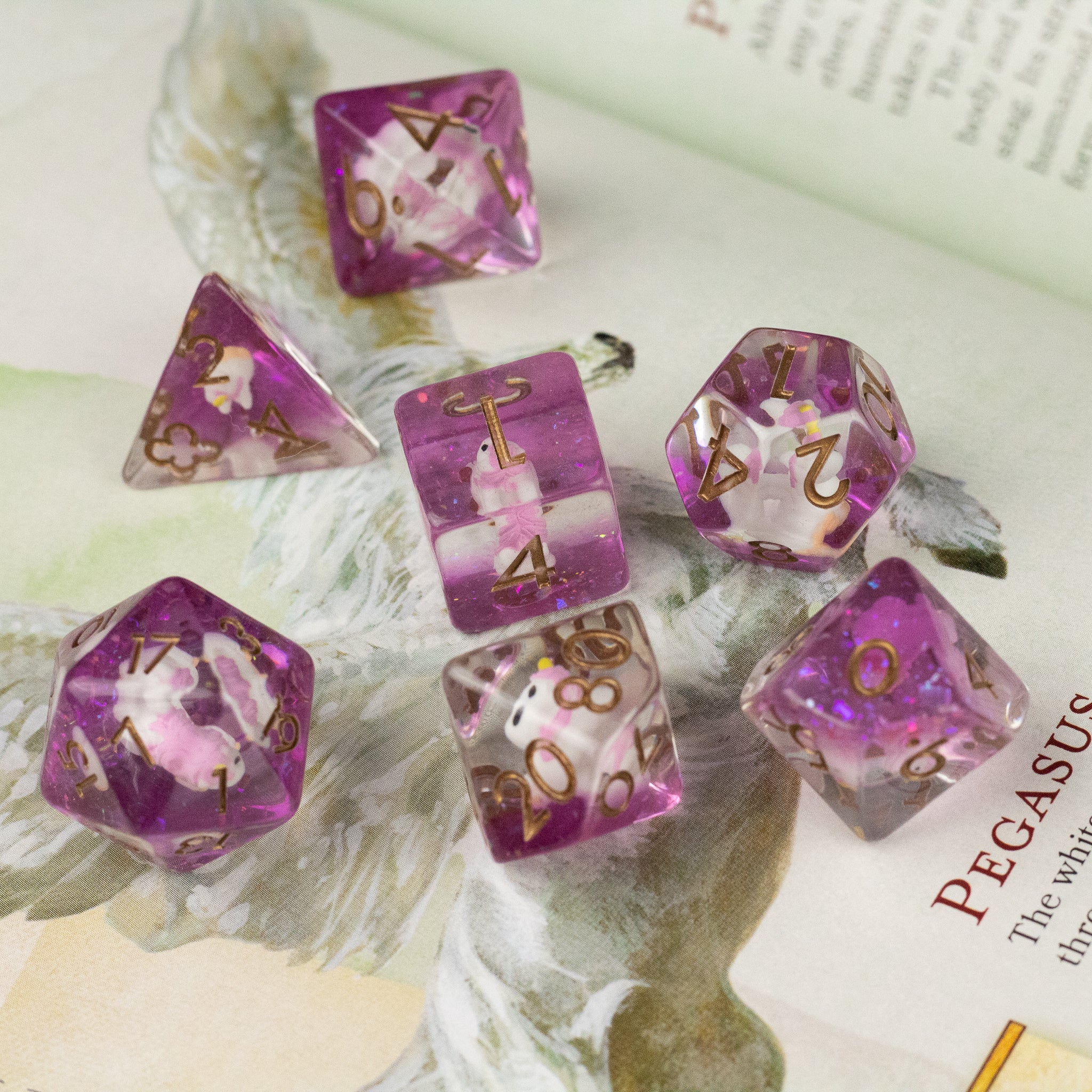 Pink Unicorn Dice Set - Seven translucent pink polyhedral dice with gold numbers, featuring a unicorn graphic inside each die.