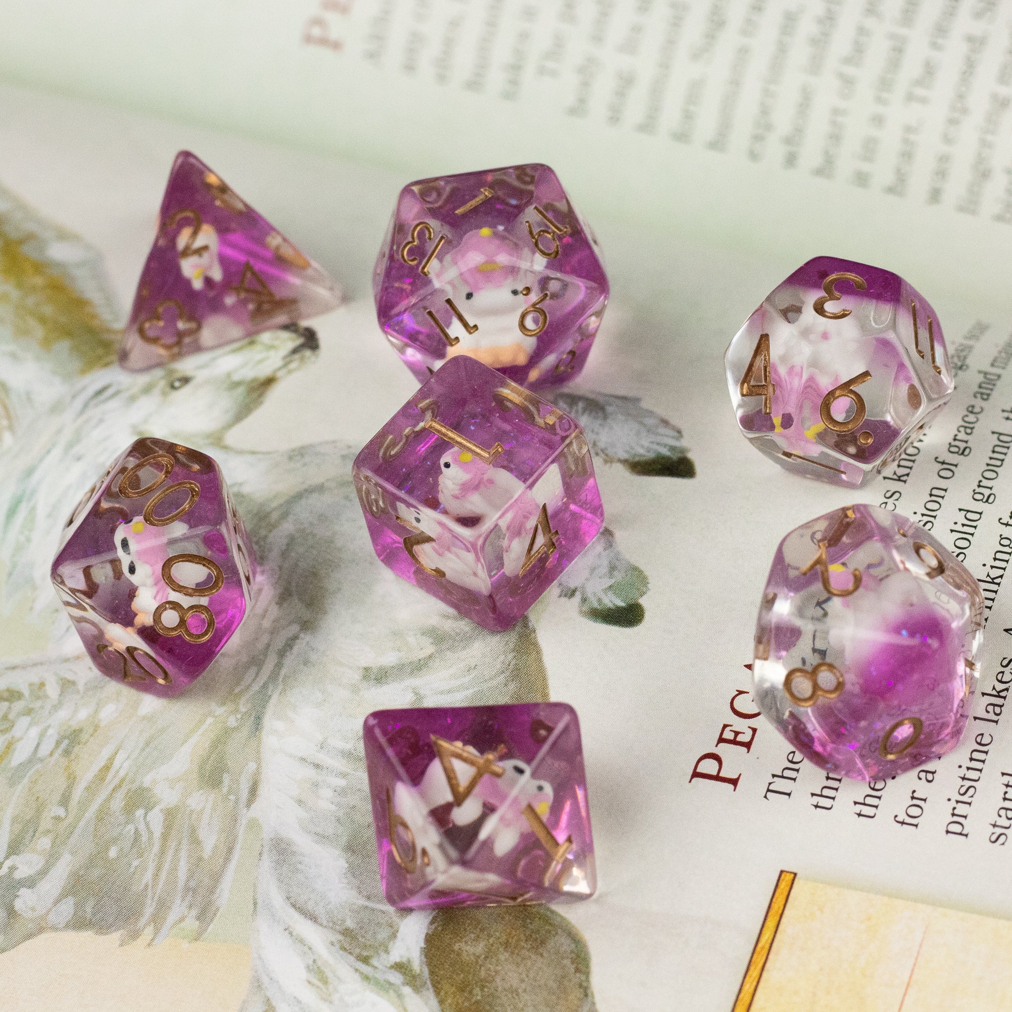 Pink Unicorn Dice Set - Set of seven translucent pink polyhedral dice with gold numbers and embedded unicorn figures.