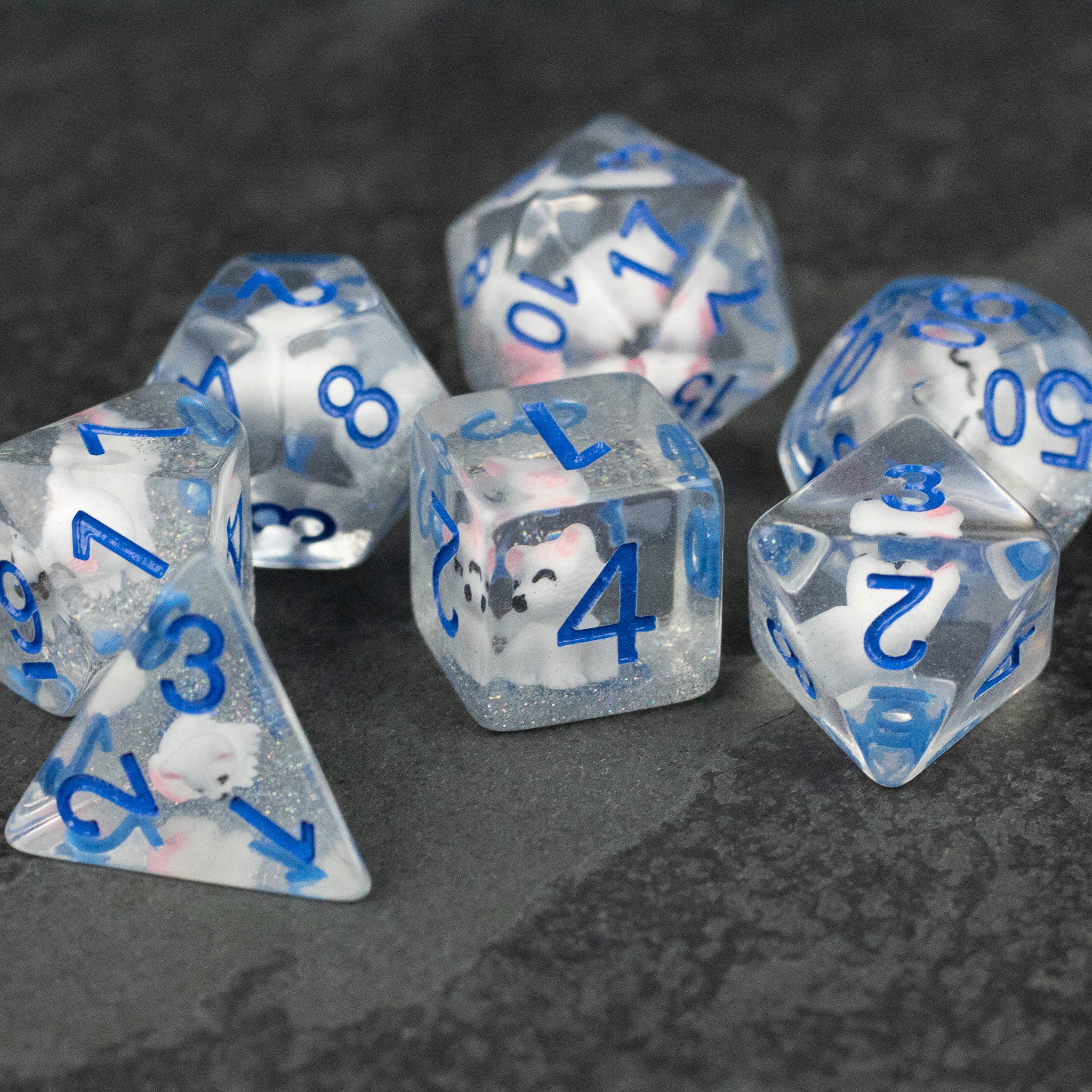 Artic Fox Dice Set - Clear dice set with blue numbers and white speckles, including d4, d6, d8, d10, d12, and d20 on dark surface.