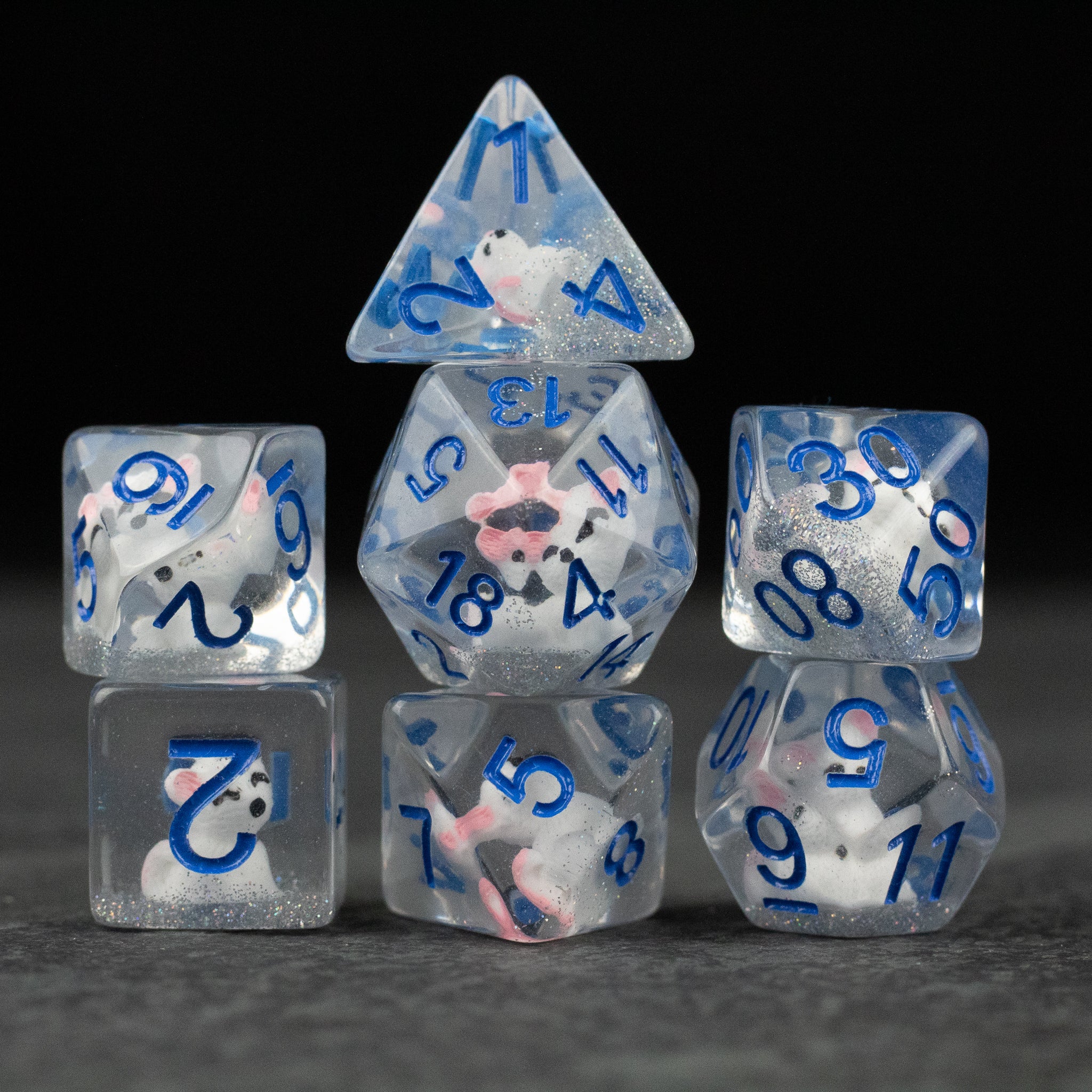 Artic Fox Dice Set - Seven transparent polyhedral dice with swirling white and pink inclusions, blue numbering, varying shapes including a.