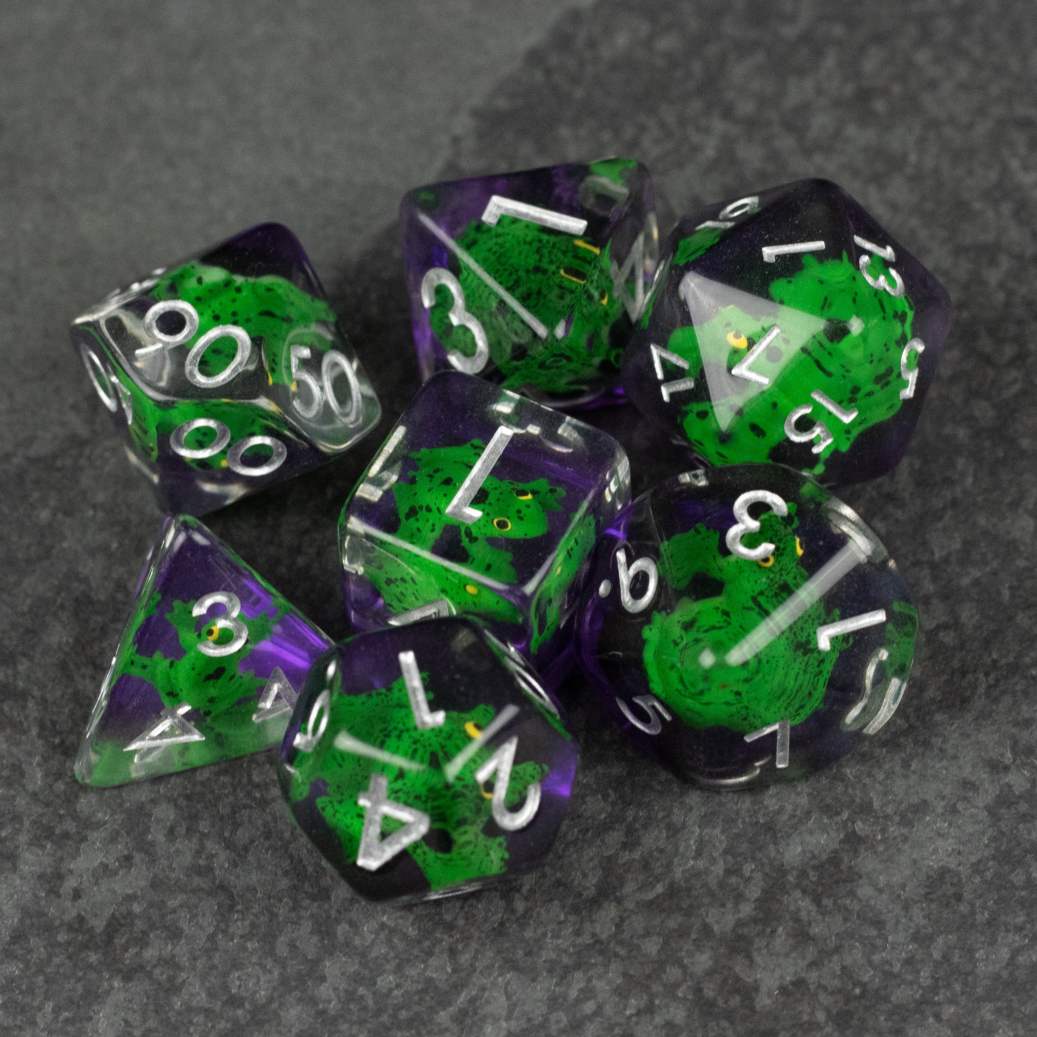 Green Frog Dice Set - Set of seven green and purple translucent polyhedral dice with white numbers on dark gray background.
