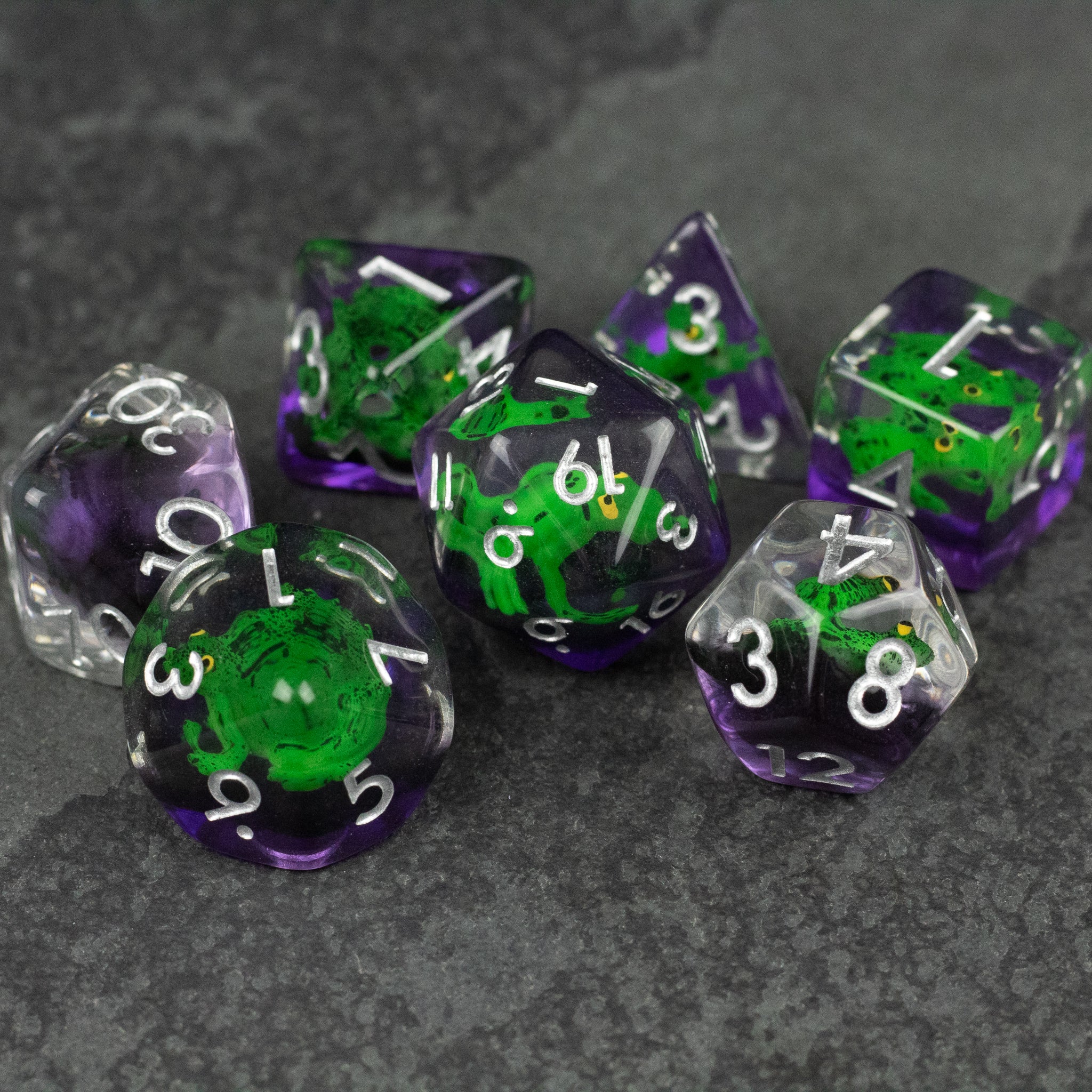Green Frog Dice Set - Set of seven translucent purple and clear polyhedral dice with detailed green frog figures inside, white numbering on each.