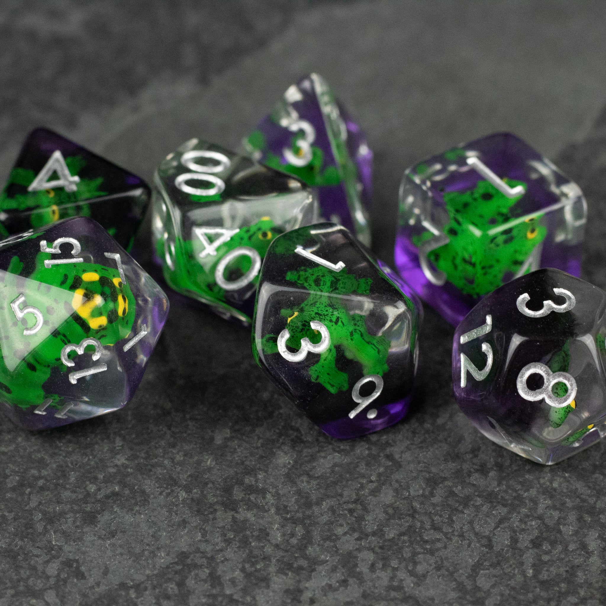 Green Frog Dice Set - Set of translucent purple polyhedral dice with green frog inclusions and white numbering.