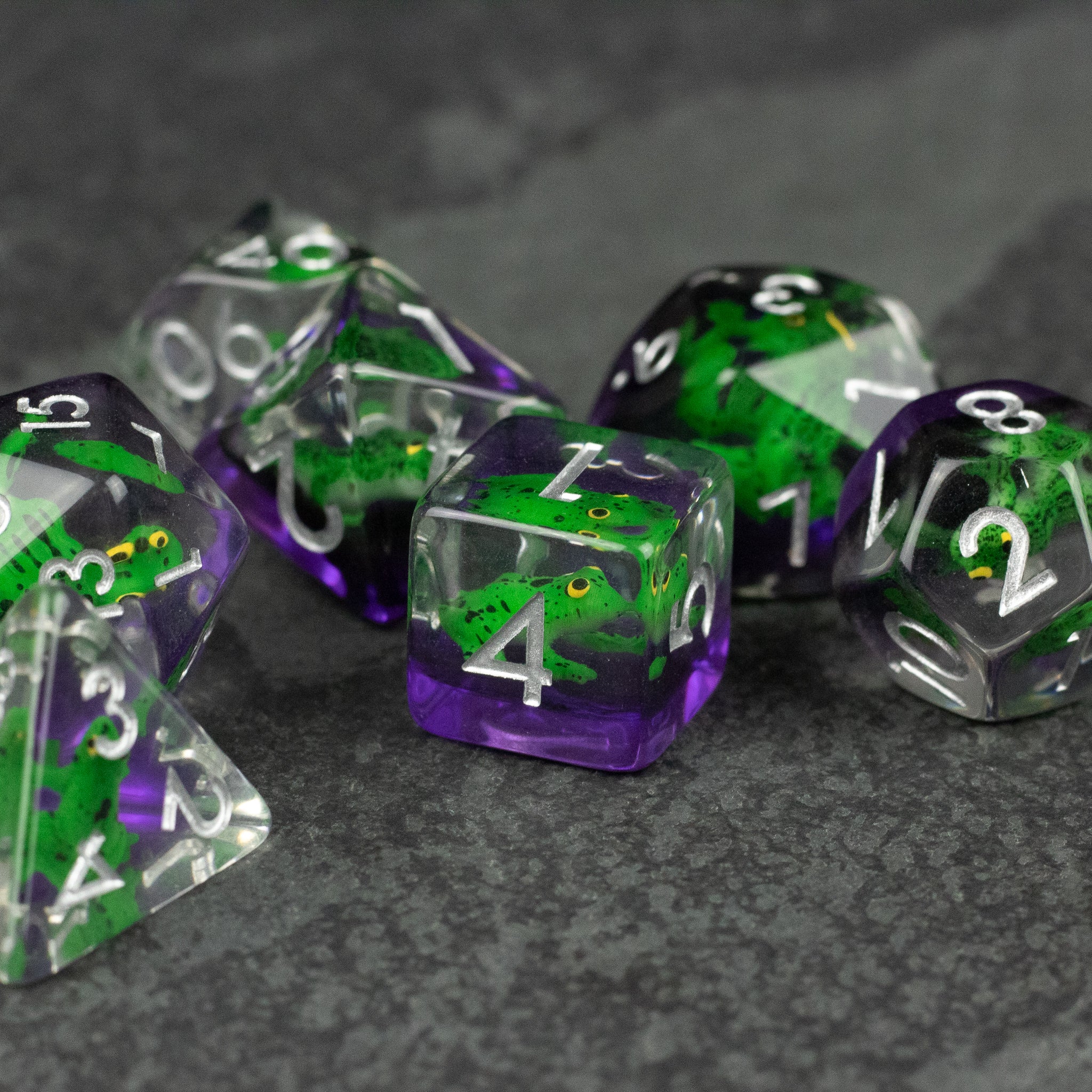 Green Frog Dice Set - Set of translucent green and purple polyhedral dice with white numbers, each containing a small green frog inside.