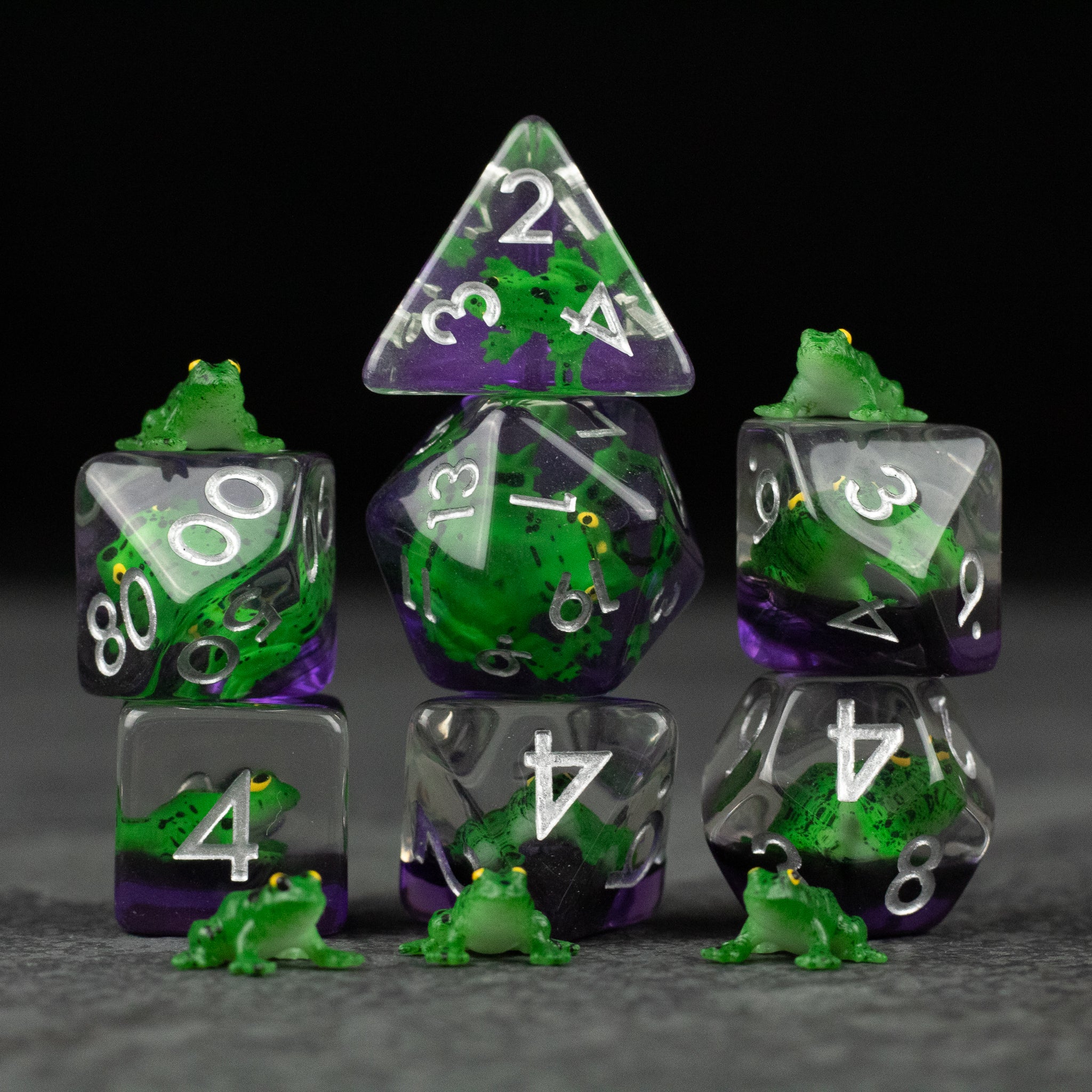 Green Frog Dice Set - Seven-piece translucent green and purple polyhedral dice set with white numbers and small green frog figurines on and around