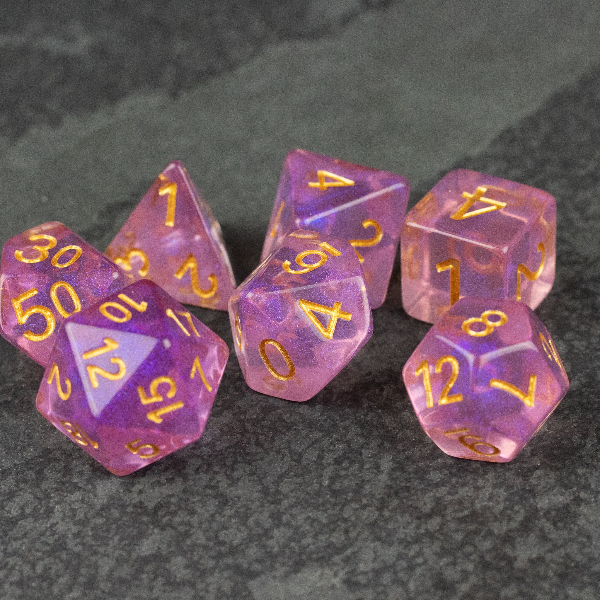 Purple Aura Glitter Dice Set - Set of seven translucent purple glitter dice with gold numbers on dark textured surface.