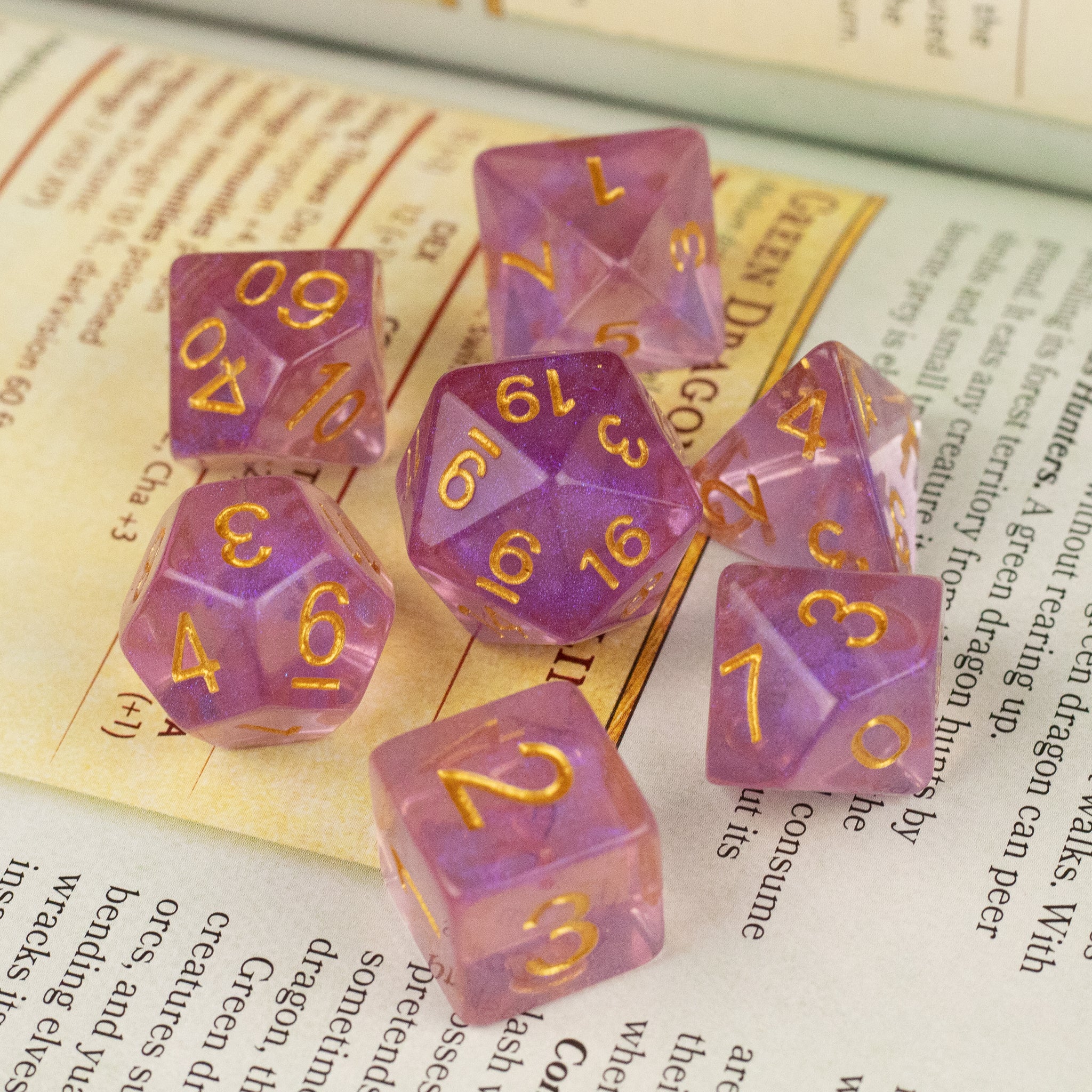 Purple Aura Glitter Dice Set - Seven-piece translucent purple glitter dice set with gold numbers on book pages.