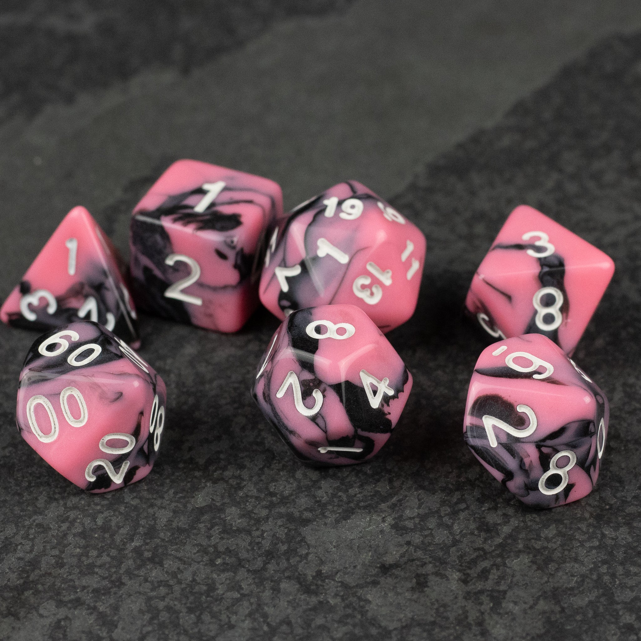 Black & Pink Marbled Dice Set - Set of seven black and pink marbled acrylic dice with white numbering on a dark textured surface.