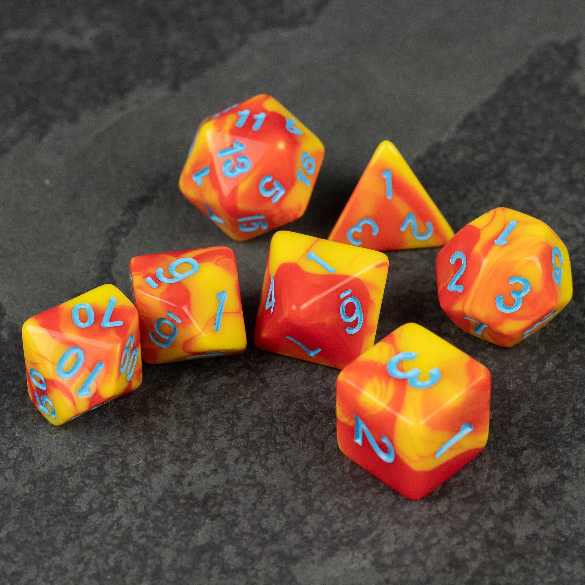 Orange & Yellow Marbled Dice Set - Seven acrylic dice with marbled orange and yellow patterns and blue numbers, including d20, d12, d10, d8, d6, and d4 shapes.