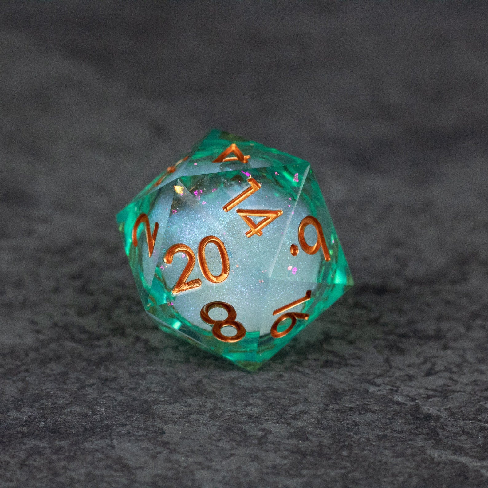 33mm Liquid Core D20 Chonk - Teal Green - Teal green 33mm D20 dice with liquid core and bronze numbers on gray surface.
