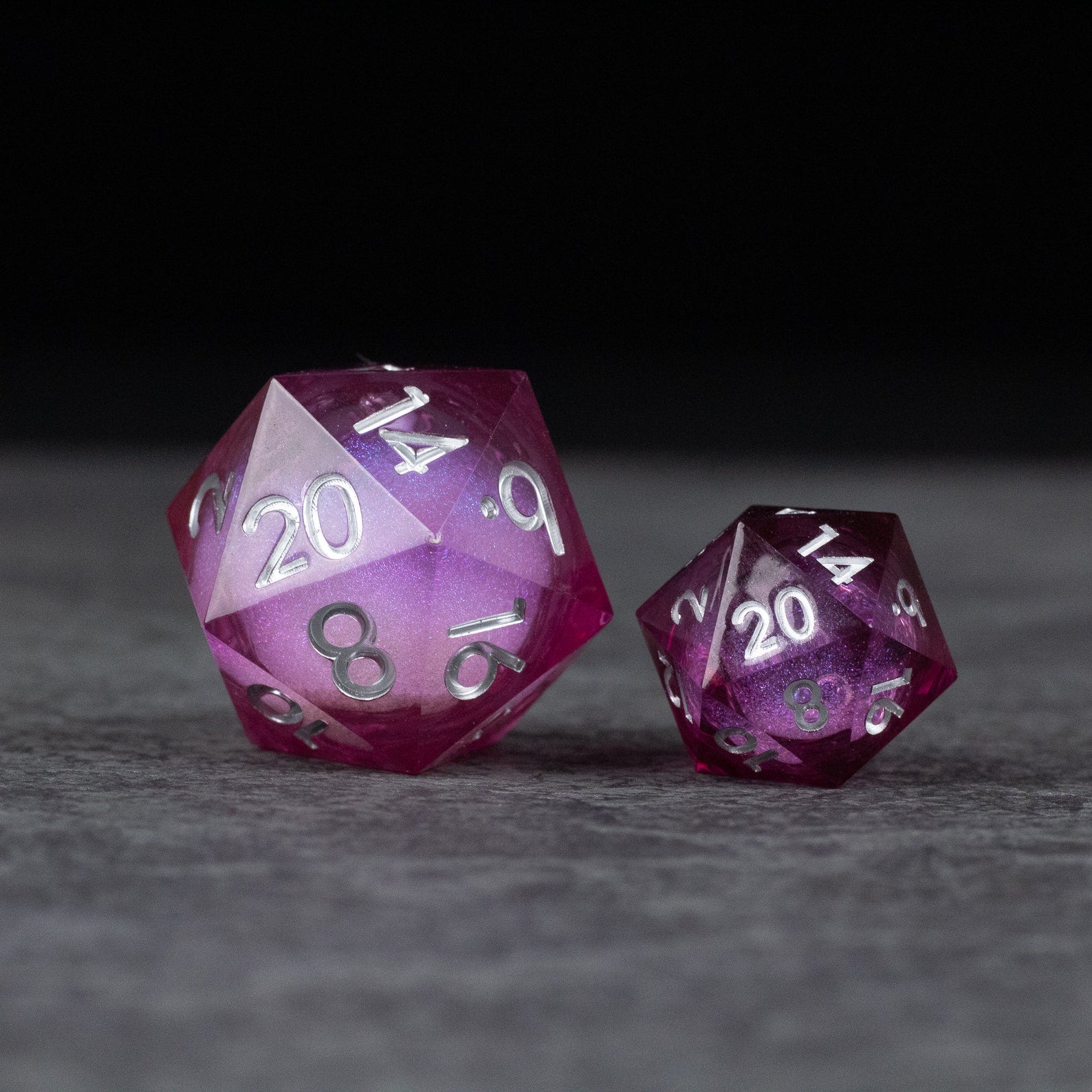 33mm Liquid Core D20 Chonk - Wine Red - Two wine red 33mm and standard-sized twenty-sided dice with liquid core and silver numbers on a gray surface.