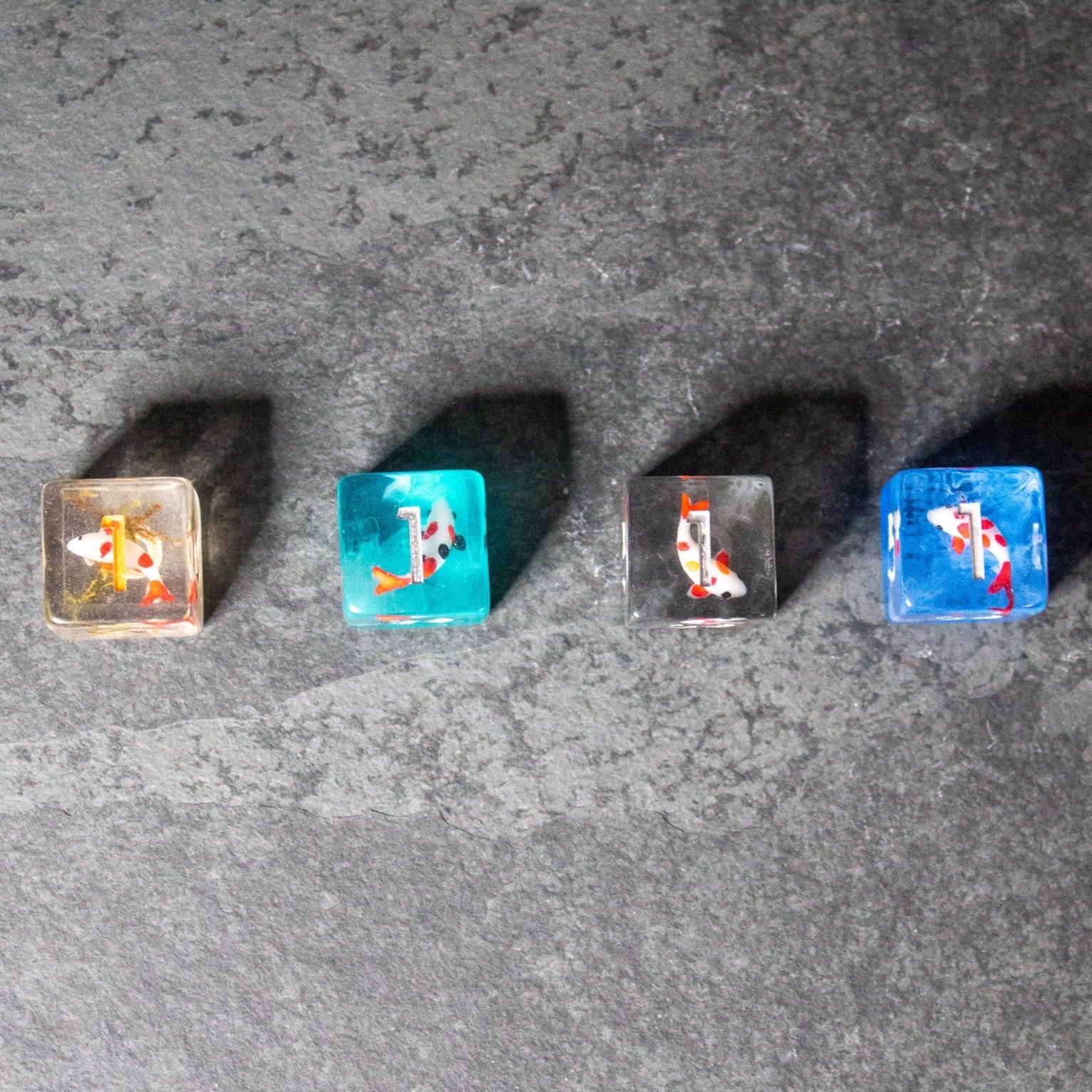 Koi Fish Dice Set - Four translucent six-sided dice in amber, turquoise, smoky gray, and royal blue, each with orange and white koi fish designs .