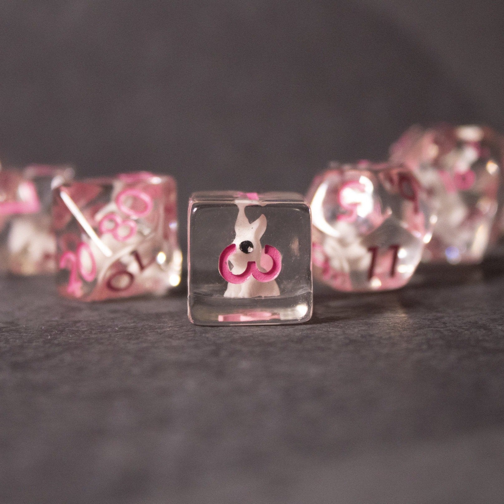 Pink Bunny Dice - Clear acrylic dice with pink bunny symbols and numbers inside, glossy finish, set on dark surface.