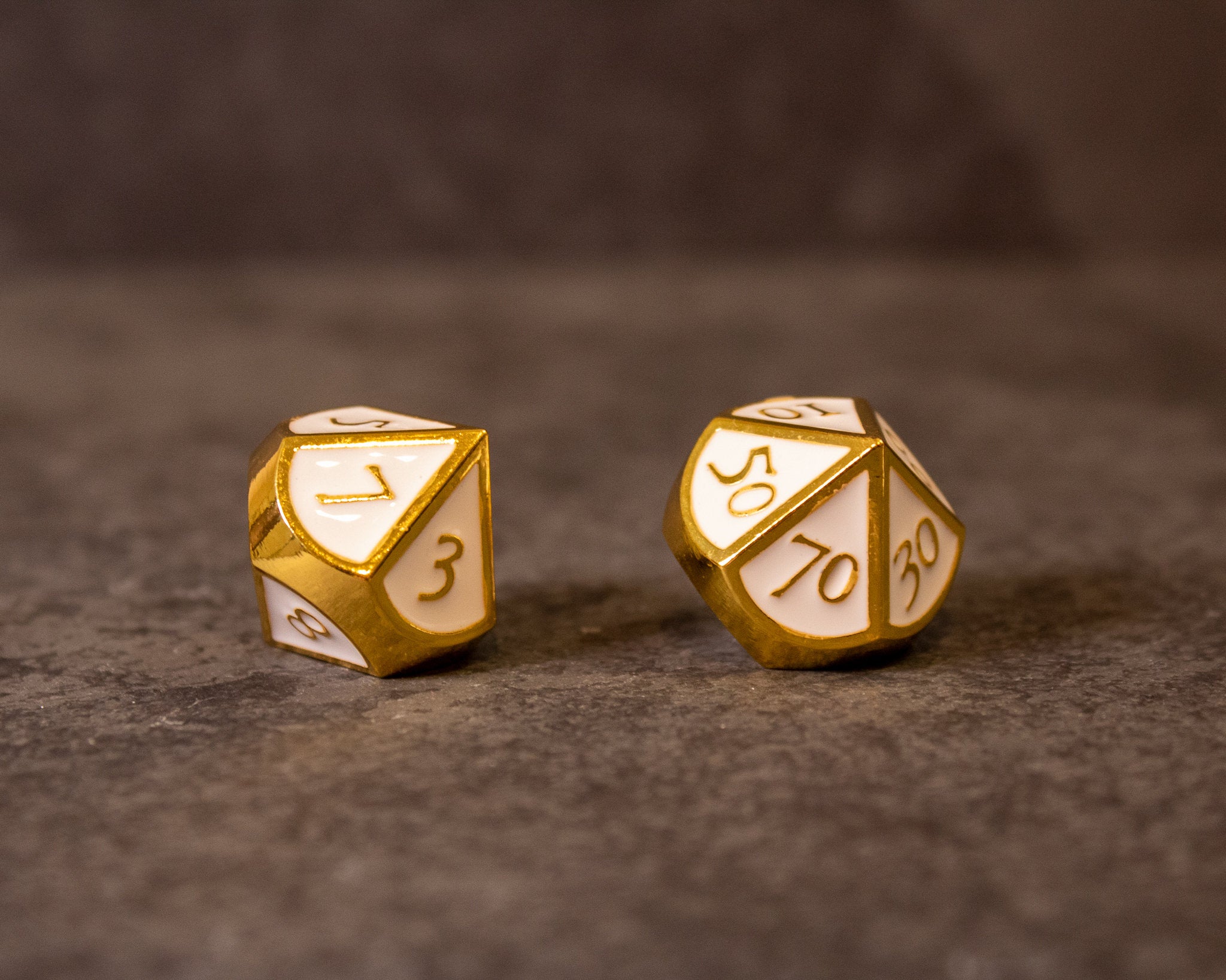 Honor - White & Gold Metal Dice - White and gold metal d20 and percentile dice with engraved numbers on a textured brown surface.