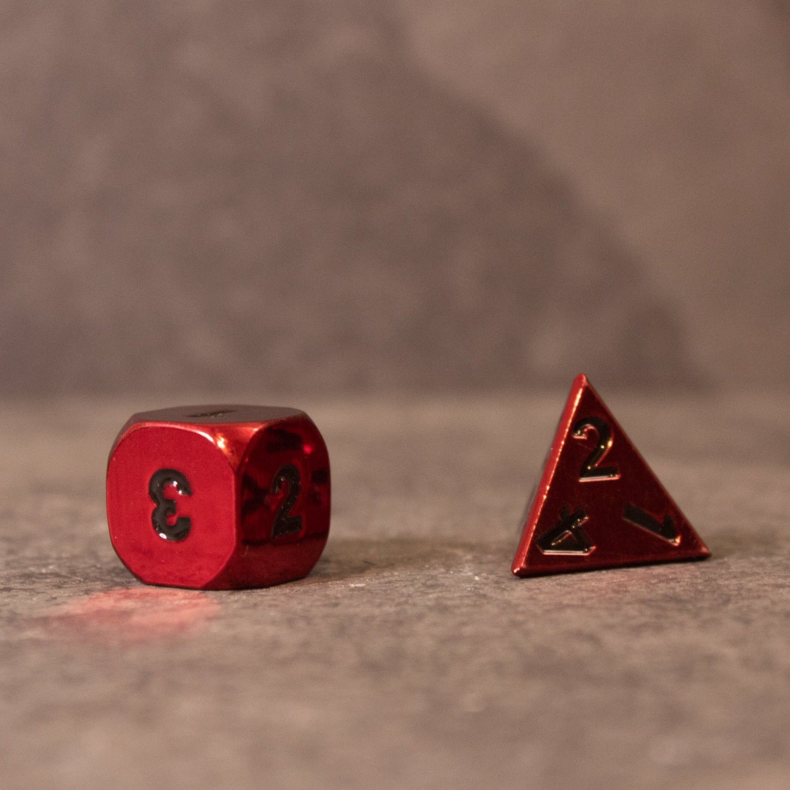 Rage - Red Metal Dice - Red metal six-sided die with black numbers and matching four-sided die with black numbers on gray surface.