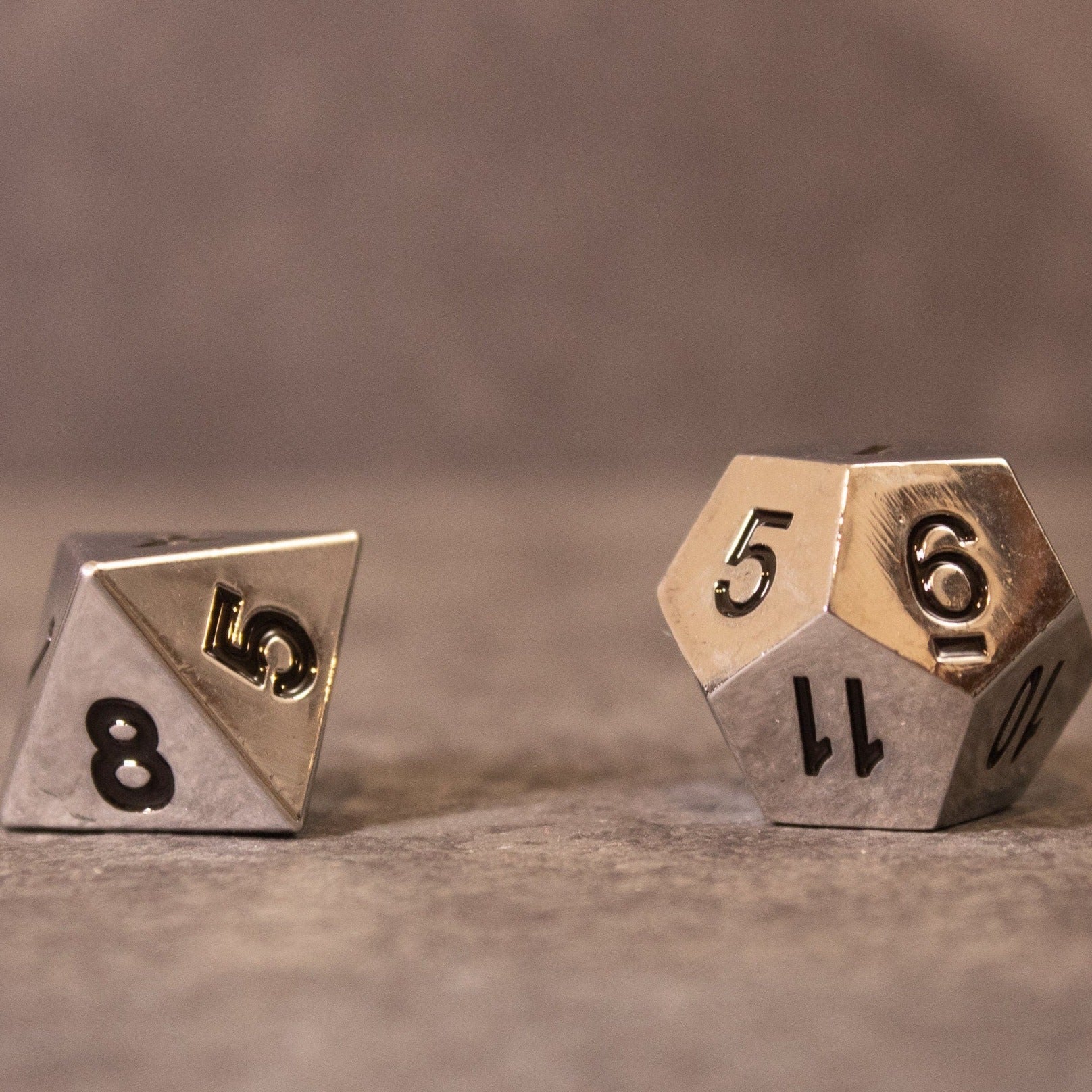 Purity - Silver Metal - Silver metal d8 and d12 dice with black numbering on a stone surface.