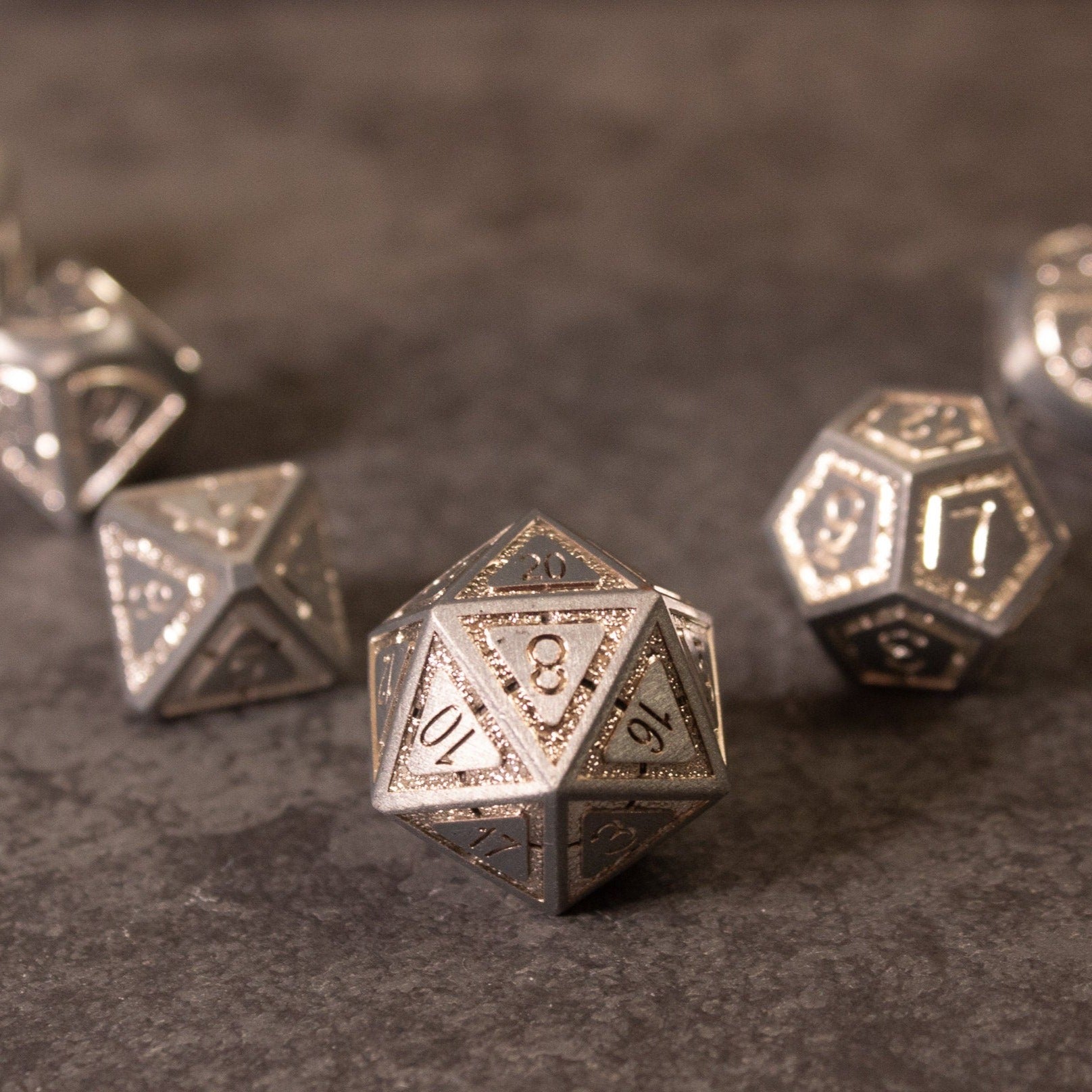 Quicksilver Core Dice Set - Set of metal polyhedral dice with etched numbers, featuring a silver-gray finish on a textured surface.