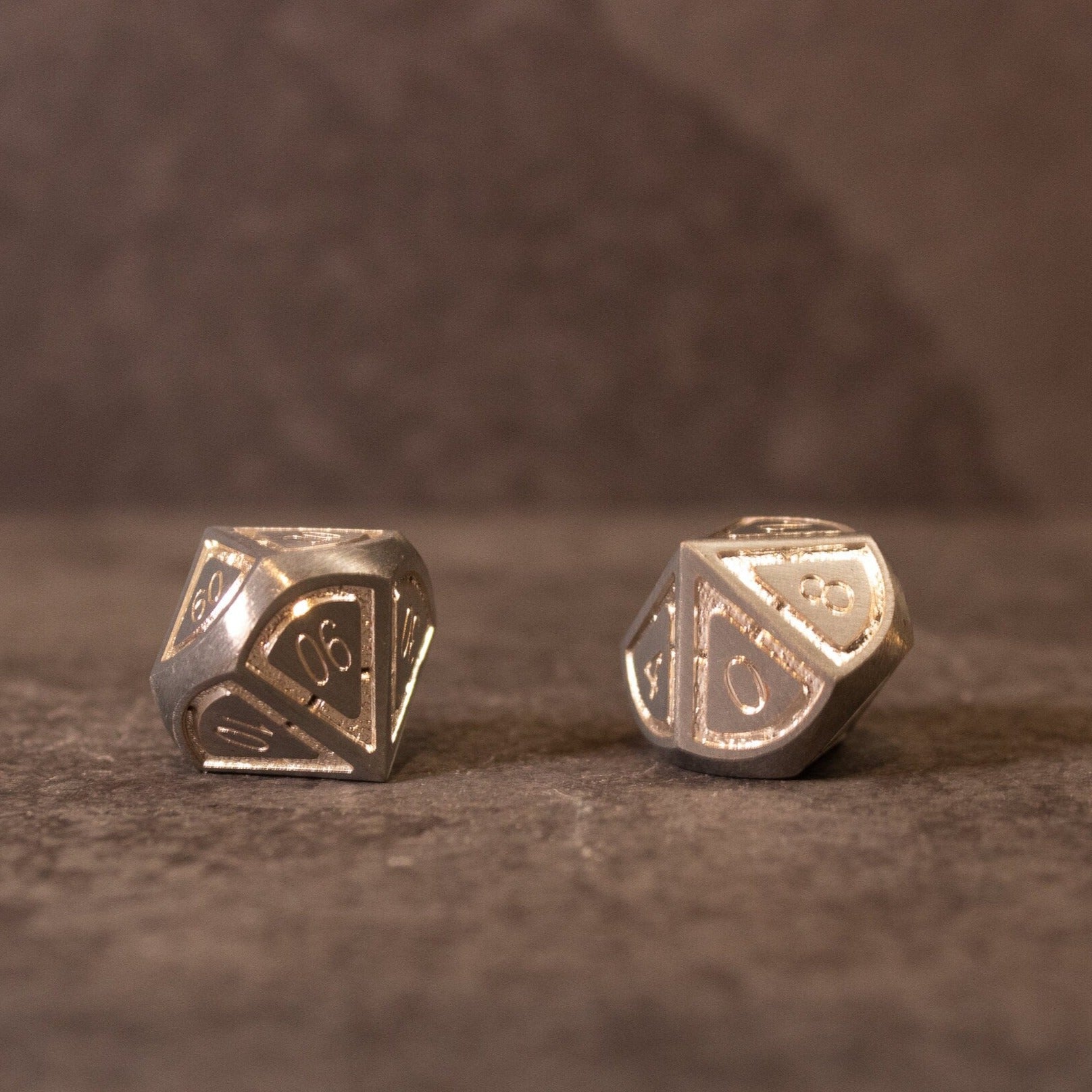 Quicksilver Core Dice Set - Two silver metal polyhedral dice with engraved numbers on a textured dark surface.