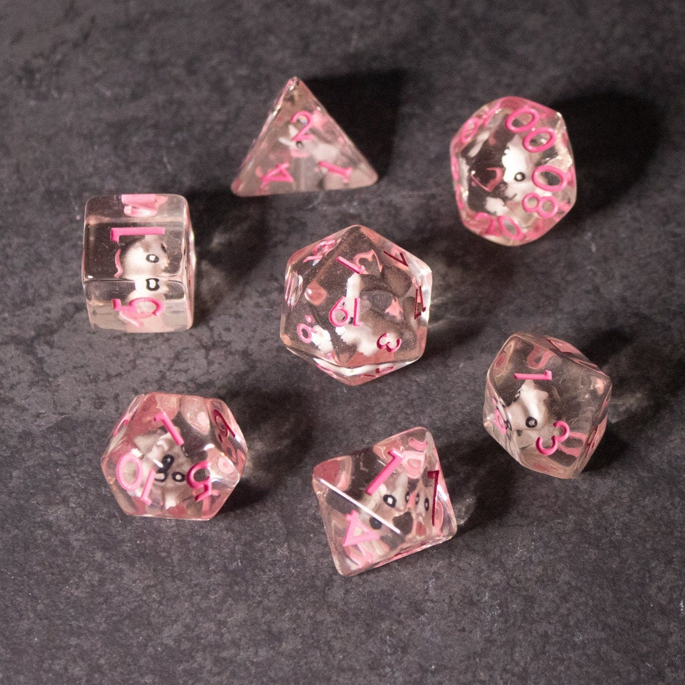 Pink Bunny Dice - Seven transparent pink polyhedral dice with white bunny icons instead of numbers on a dark textured surface.