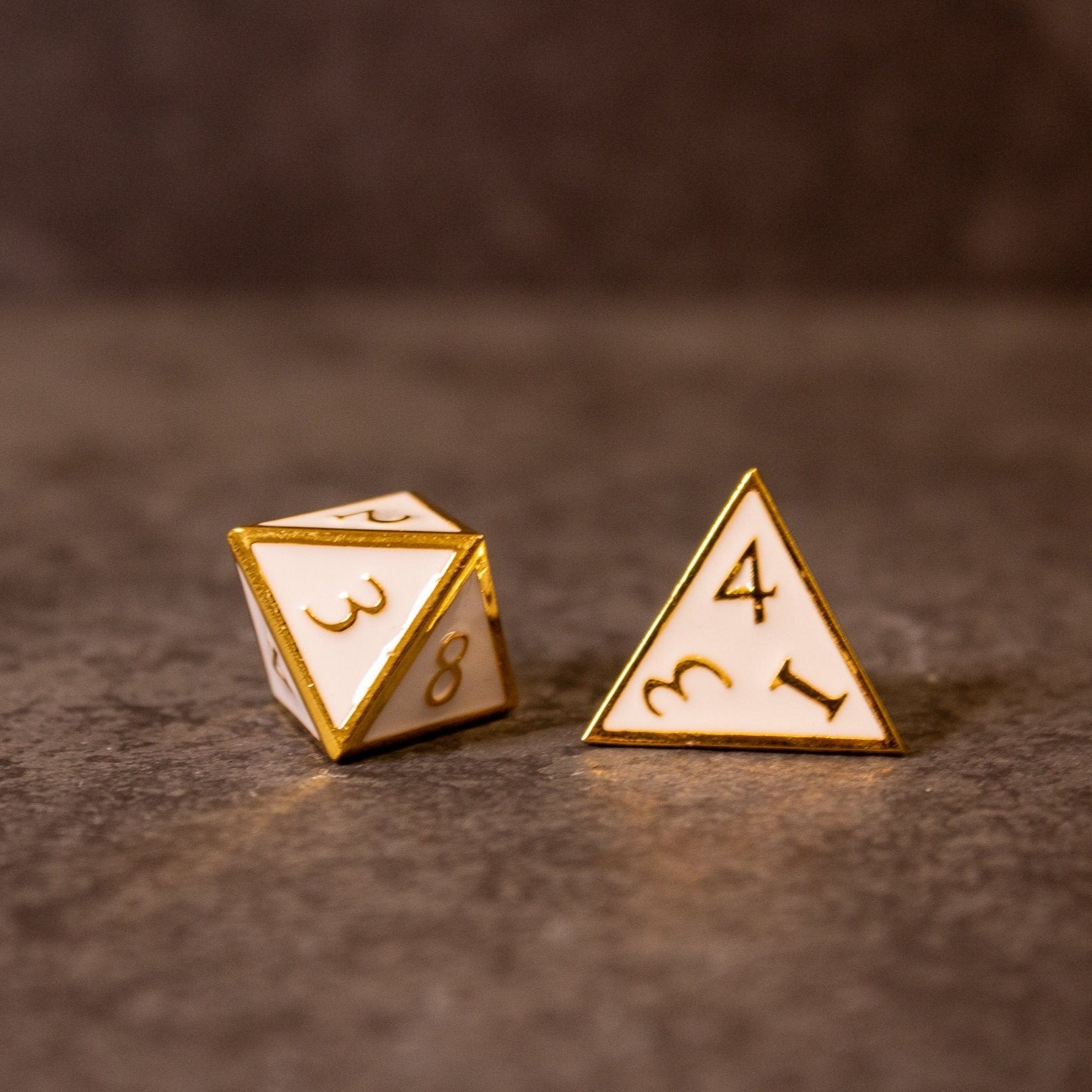 Honor - White & Gold Metal Dice - White metal dice with gold edges and engraved numbers, showing a four-sided and an eight-sided die on a brown surface.
