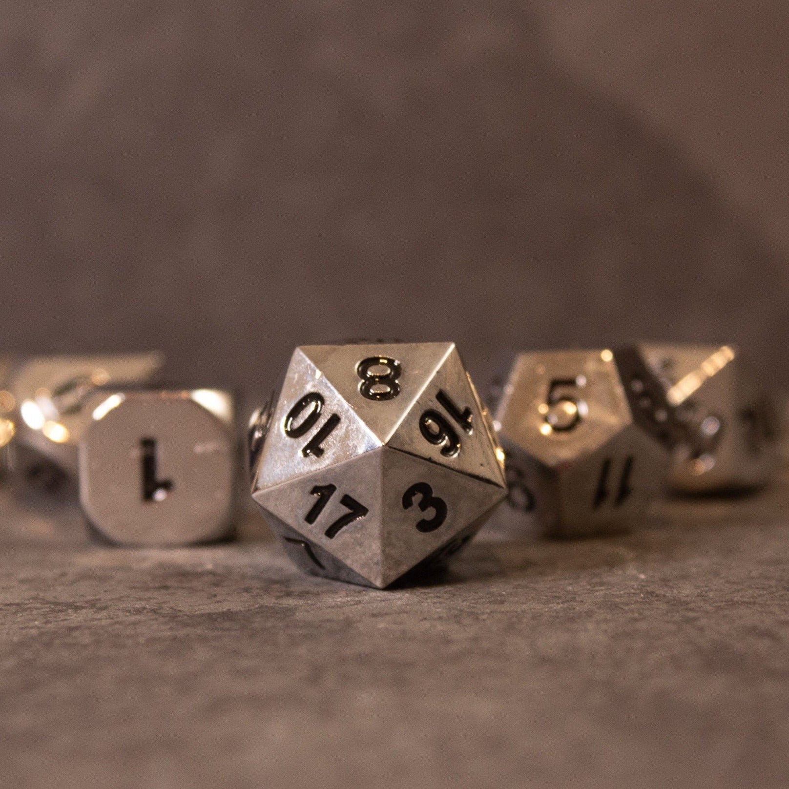 Purity - Silver Metal - Silver metal 20-sided die with black numbers surrounded by other silver metal dice on a brown surface.