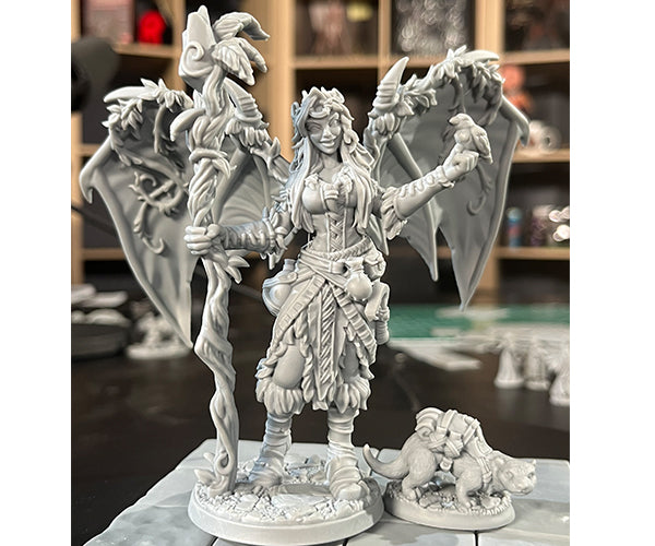 Druid Sophie with Ottley - Gray unpainted fantasy figurine of a druid woman with detailed armor and leaves, standing next to a large dragon with spread