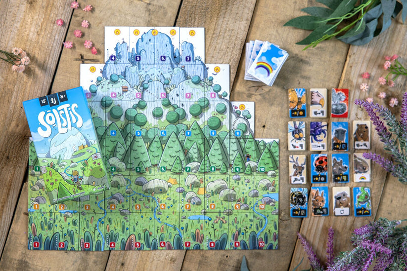 Solstis - Colorful board game with illustrated forest and mountain landscape, cards featuring animal characters, and a game booklet.