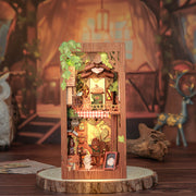 Squirrel Collector Book Nook (PREORDER) - Wooden vertical book nook featuring a miniature woodland house with warm lights, greenery, and tiny squirrel figurines.