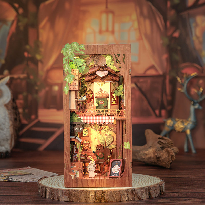 Squirrel Collector Book Nook (PREORDER) - Wooden vertical book nook featuring a miniature woodland house with warm lights, greenery, and tiny squirrel figurines.