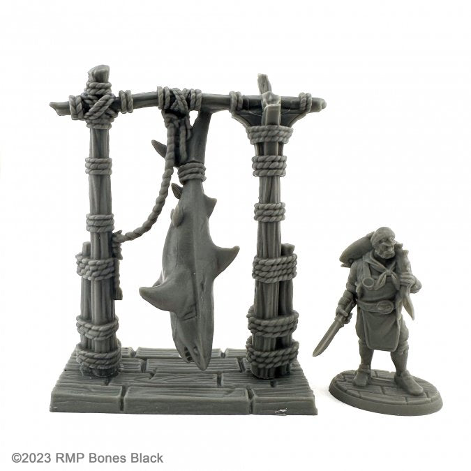 Shark Butcher - Gray resin miniature of a shark hanging from a wooden frame tied with ropes, next to a cloaked figure holding a cleaver.